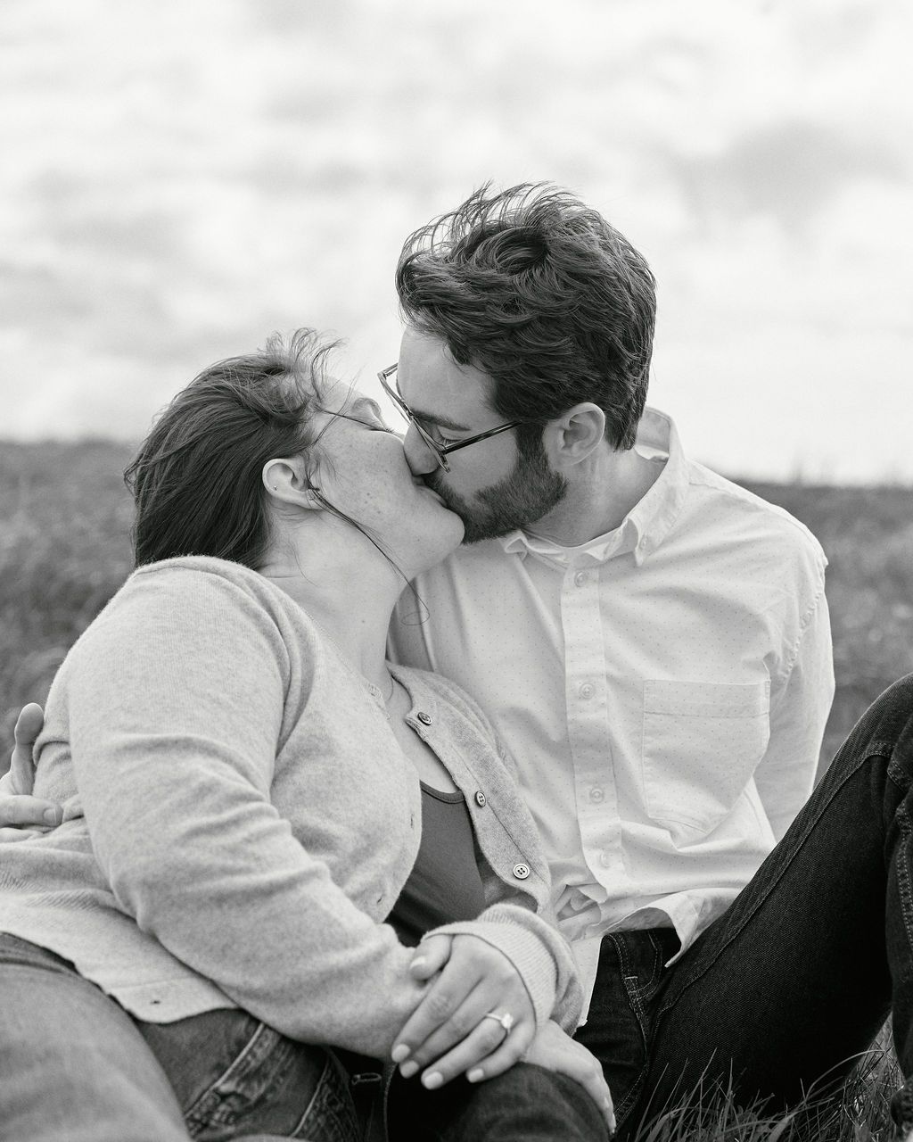 A romantic black and white portrait of a couple sharing an intimate kiss while sitting together outdoors.