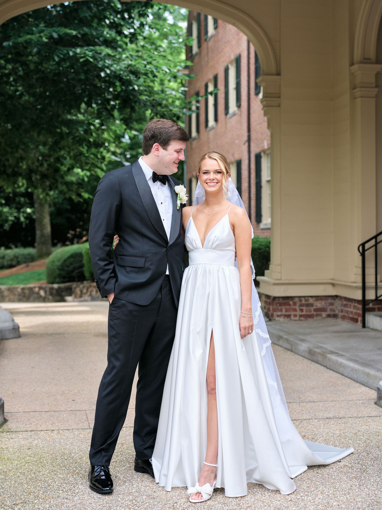 A stylish bride in a white split gown poses with her groom in classic black tie attire.