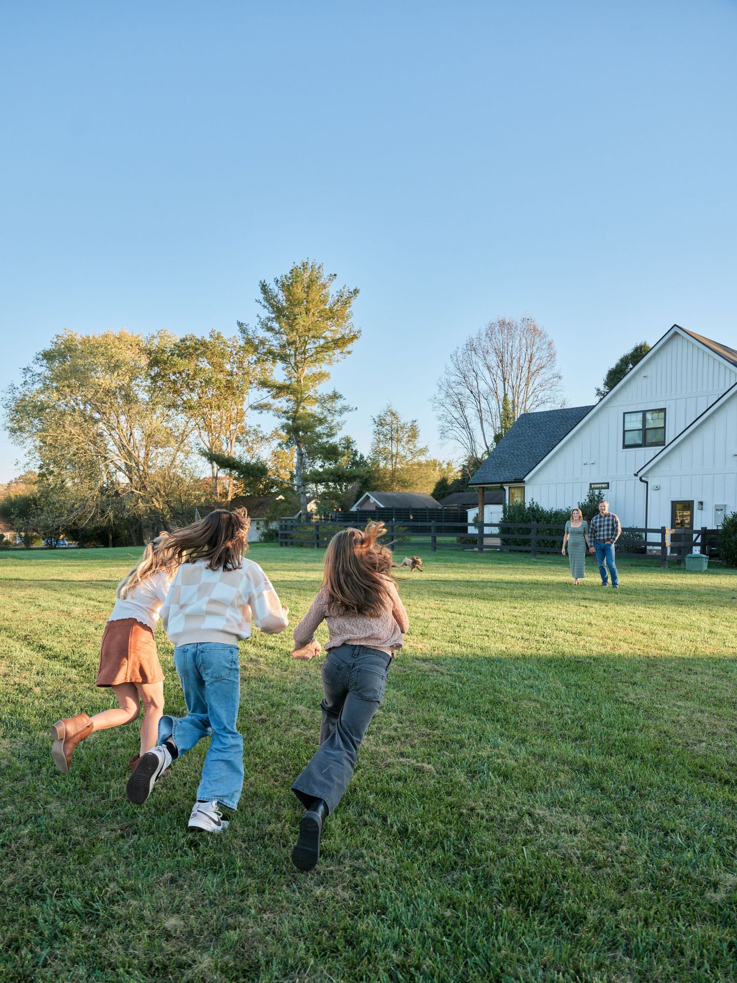 A sequence of photos shows three people running and playing together on a grassy hillside near a white barn building.