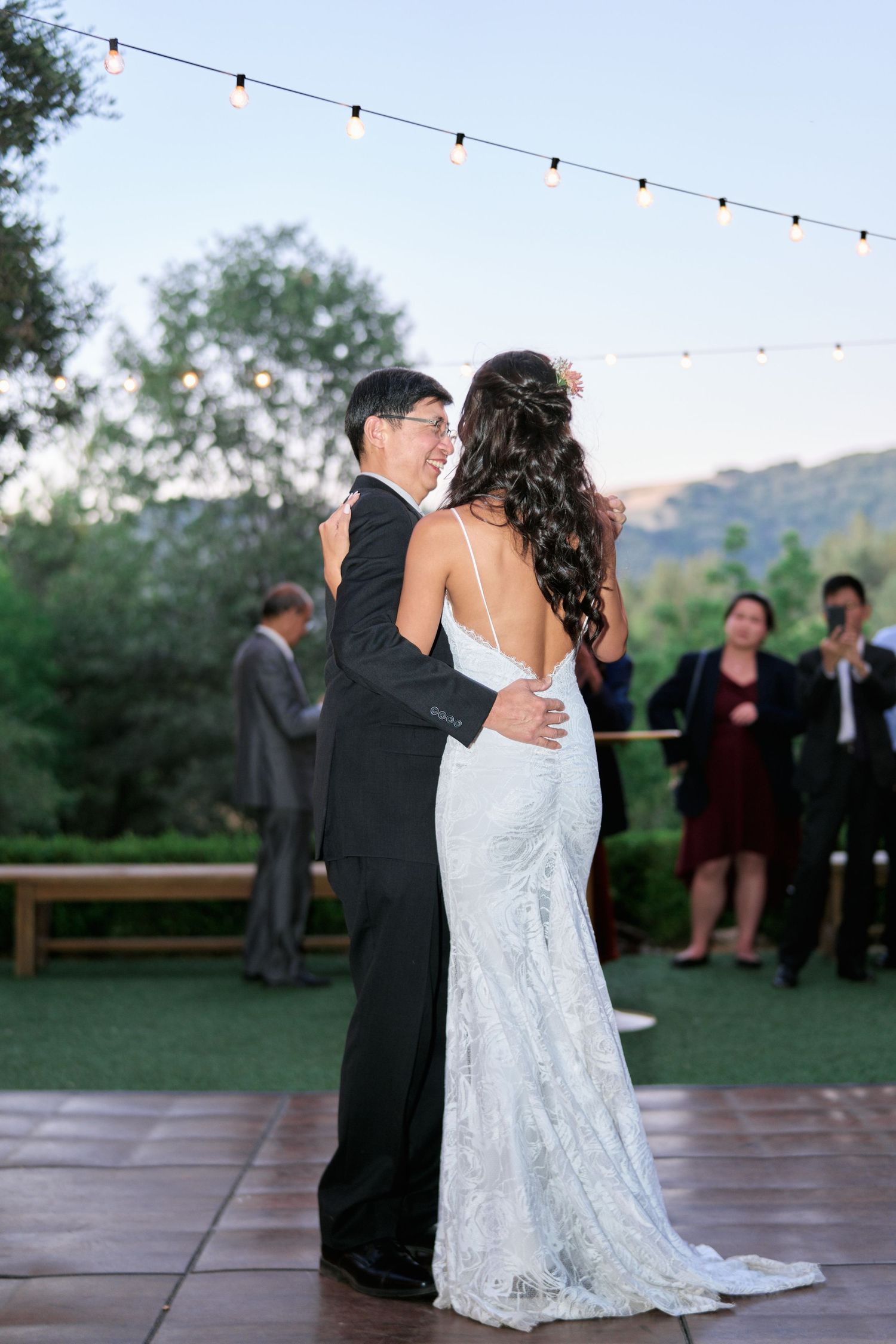 Newlyweds share a romantic dance on an outdoor patio with string lights and mountain views.