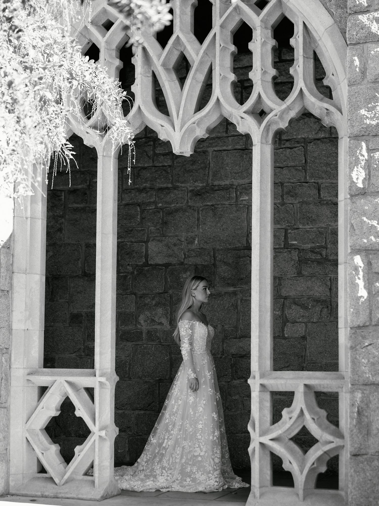 Romantic bridal portrait framed by ornate gothic stone archways in black and white.