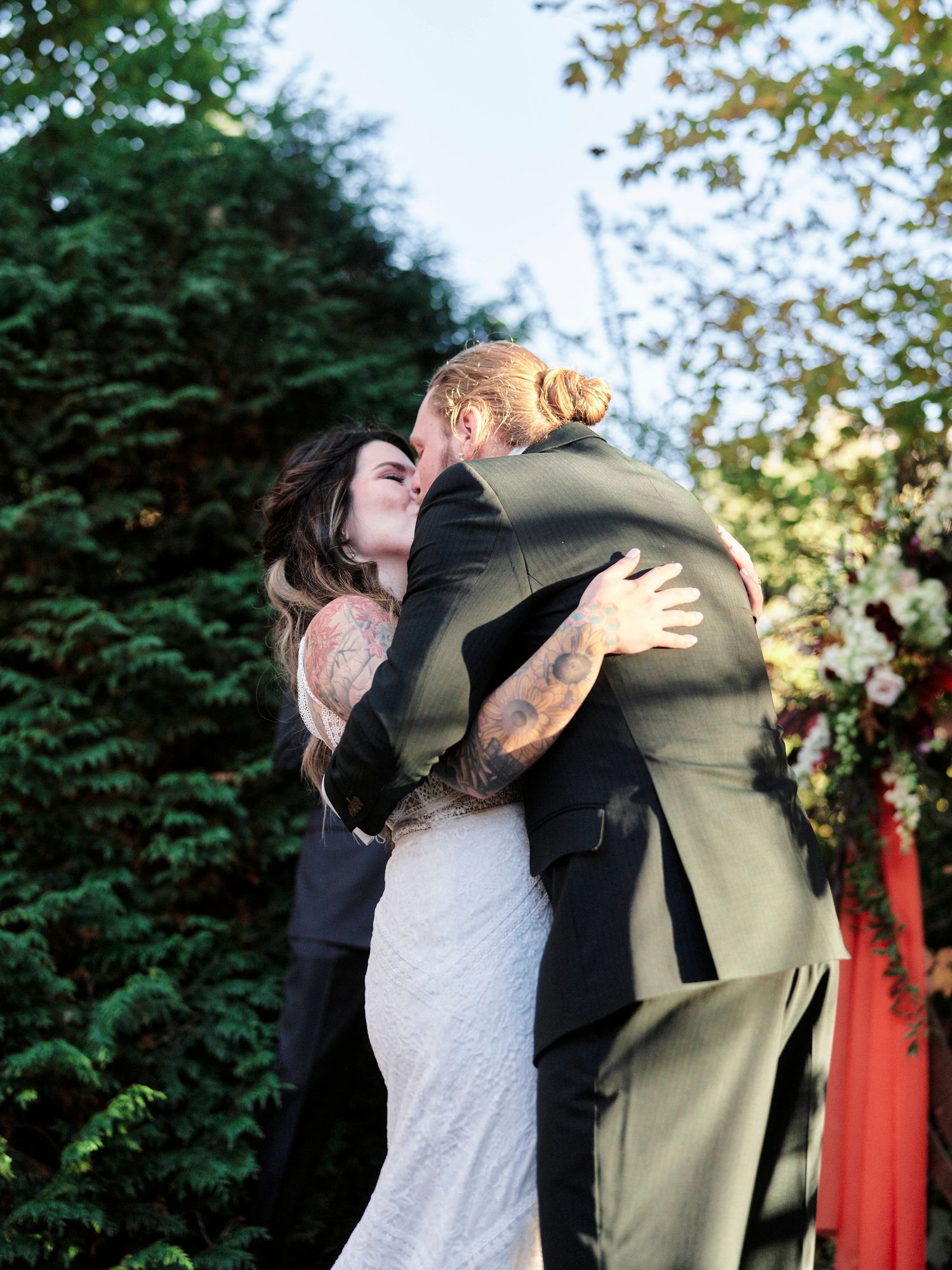 A couple shares a joyful embrace under autumn trees at their outdoor wedding celebration.