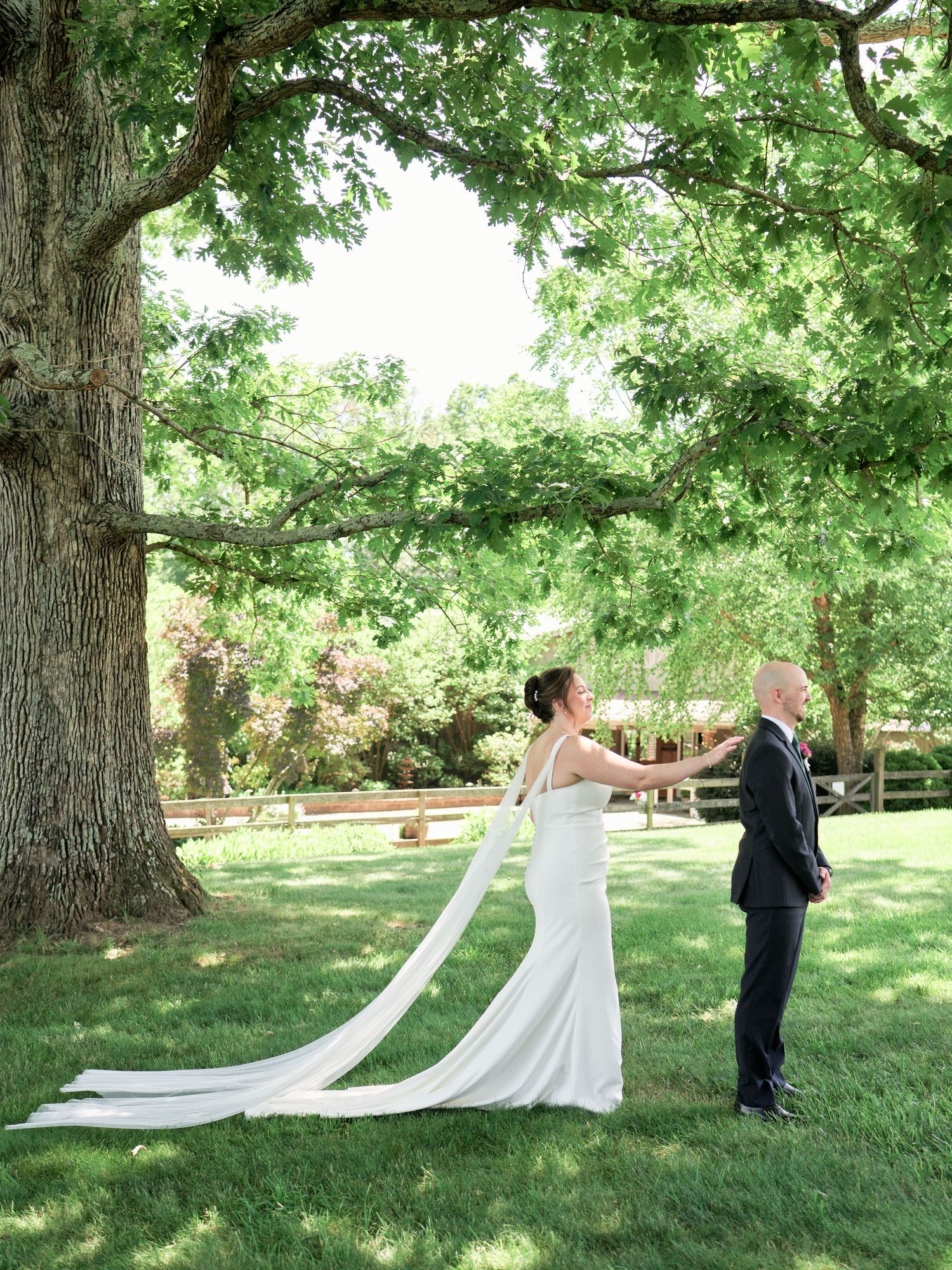 A couple poses in a creative first look photo under a large tree on their wedding day.