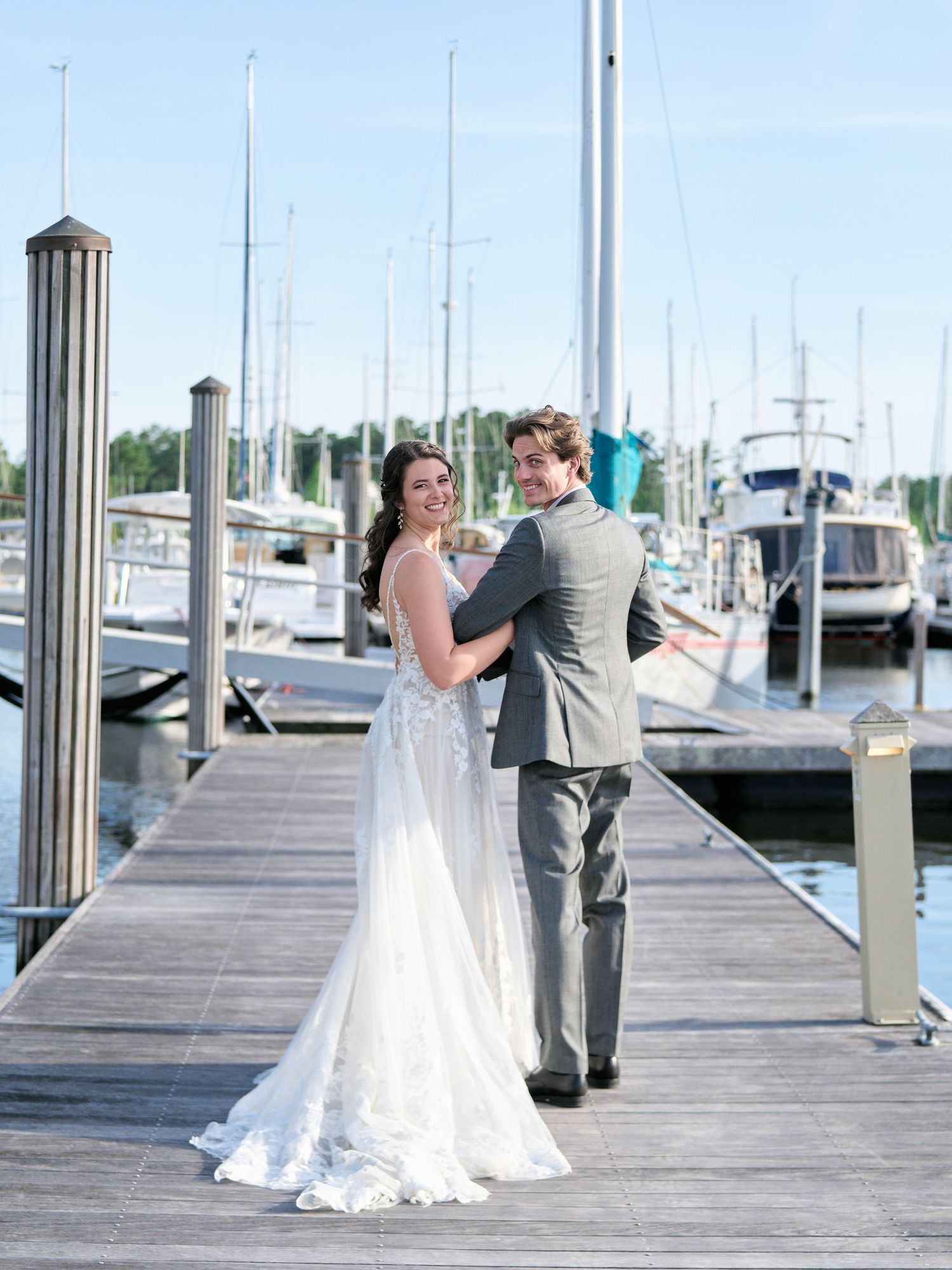 A couple shares a romantic moment on a wooden dock at a marina surrounded by boats on a sunny day.