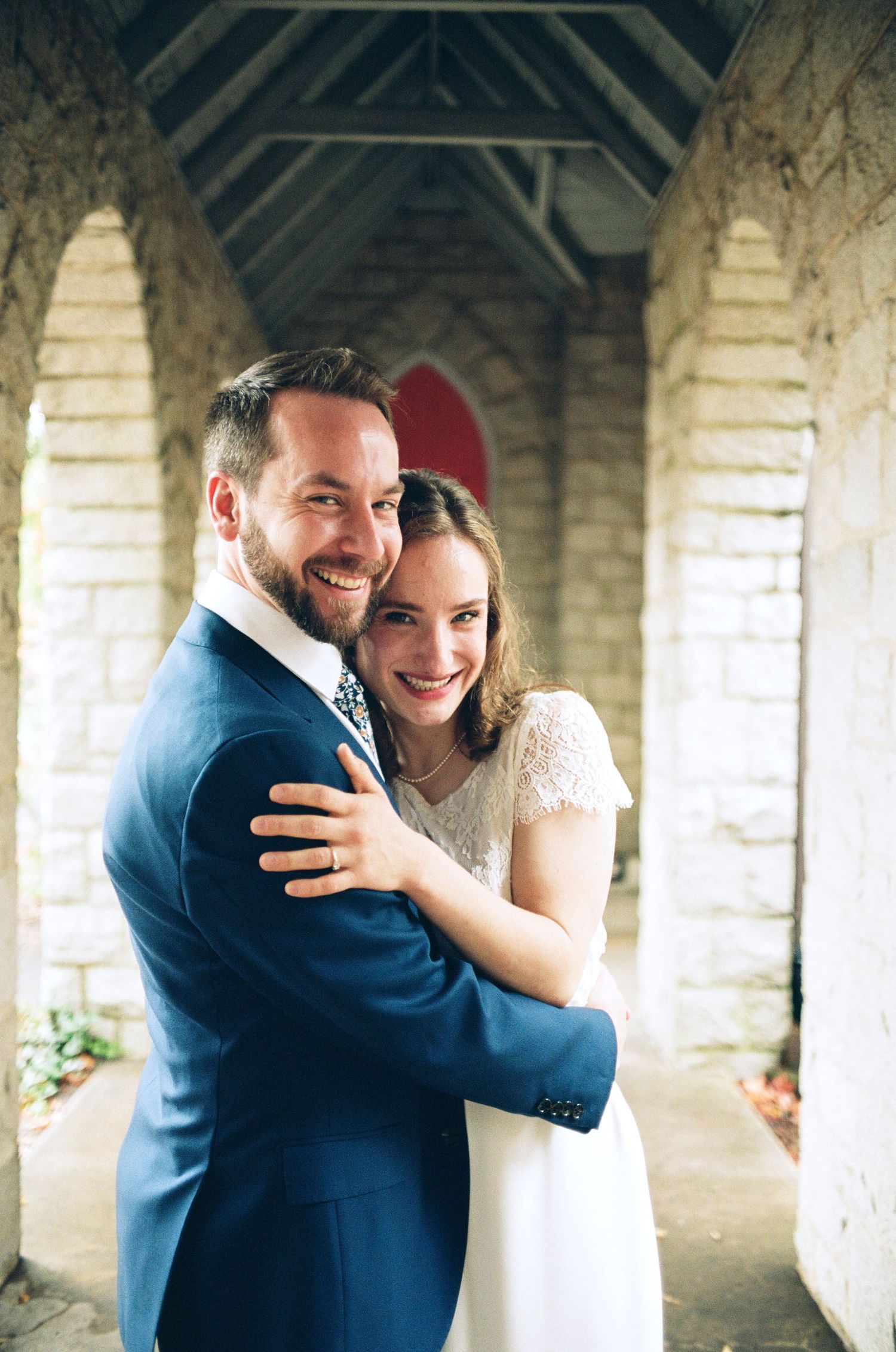 A joyful embrace captured between stone pillars with a red door in the background.