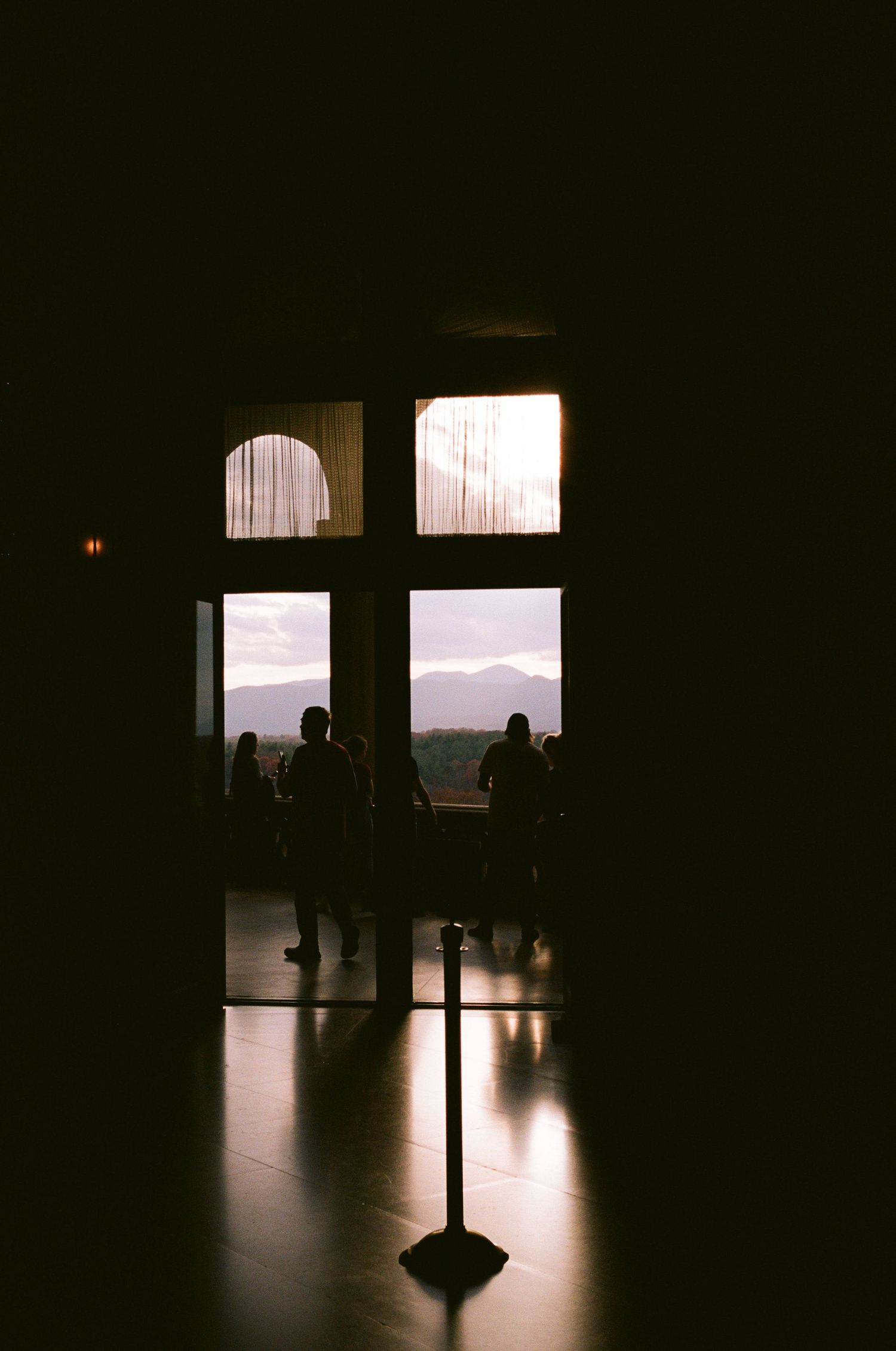 Silhouettes against large windows at sunset in dark interior space.