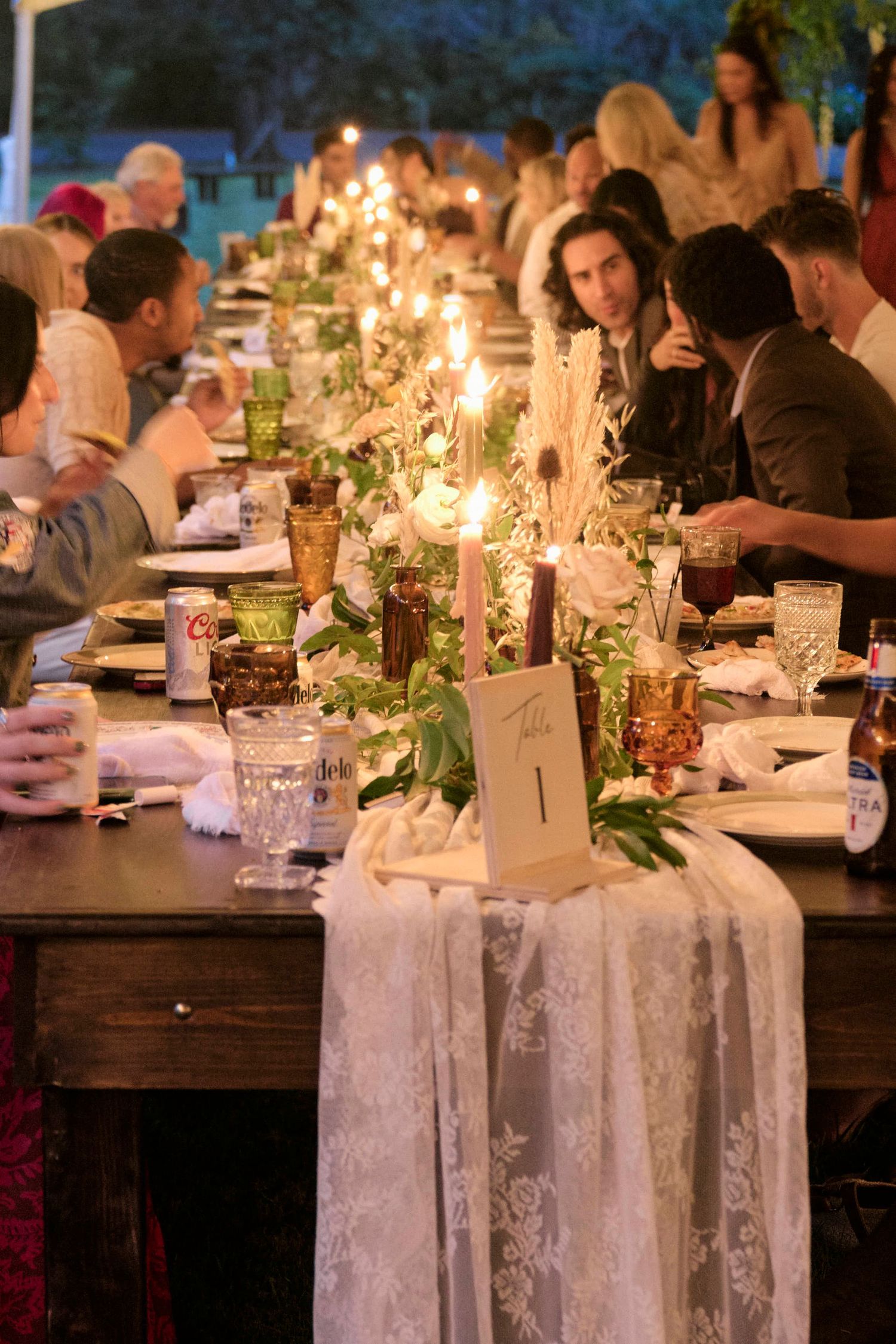 An elegant candlelit wedding reception table decorated with greenery and lace runners.