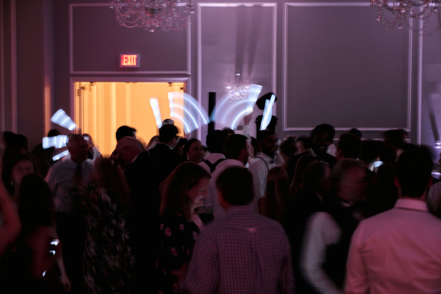 A crowd of party guests dancing under purple lighting at an evening celebration.