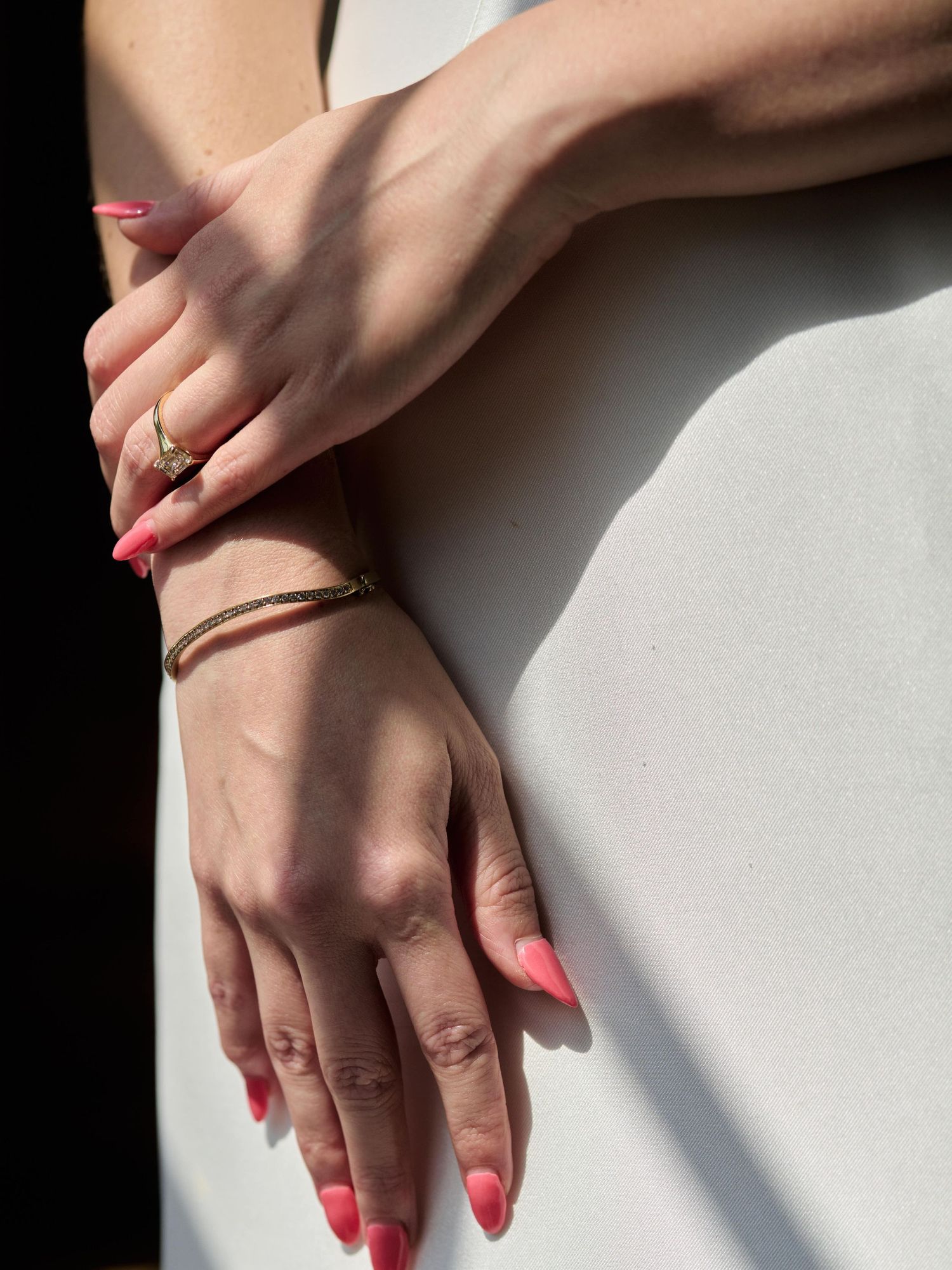 Hands with coral nail polish and delicate jewelry against white background in dramatic lighting.
