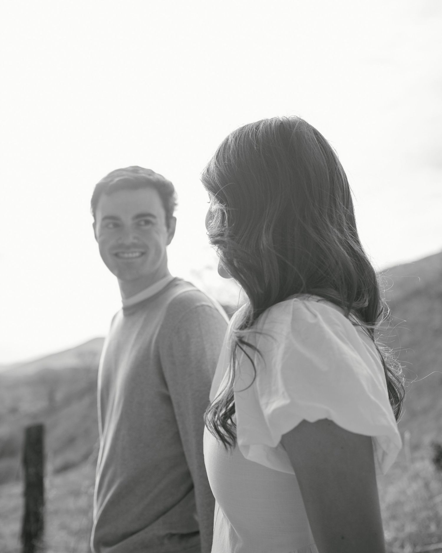 A romantic black and white photo series showing a couple laughing and embracing on a hillside.