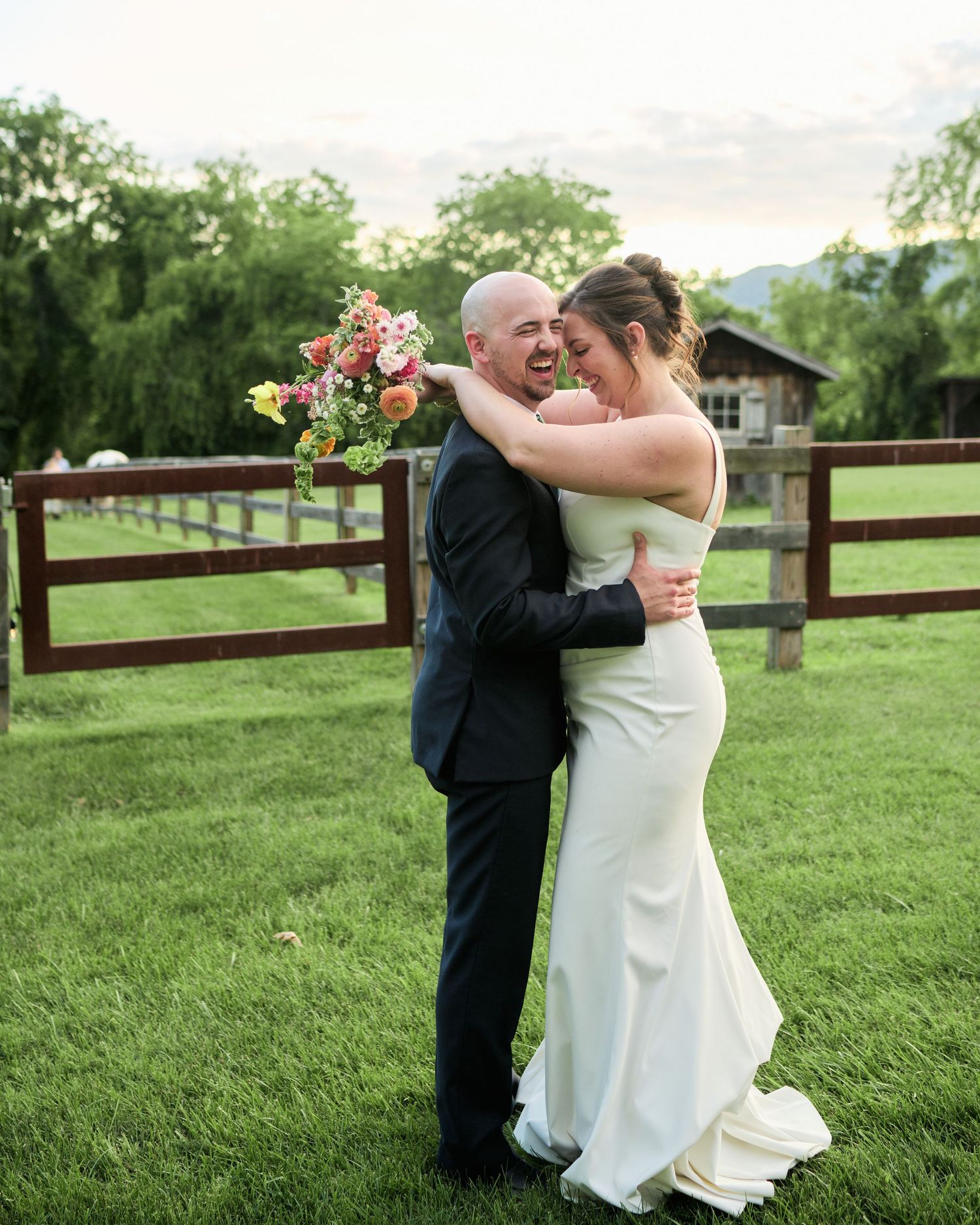A couple shares a romantic dance moment on a grassy lawn with wooden fencing in the background.