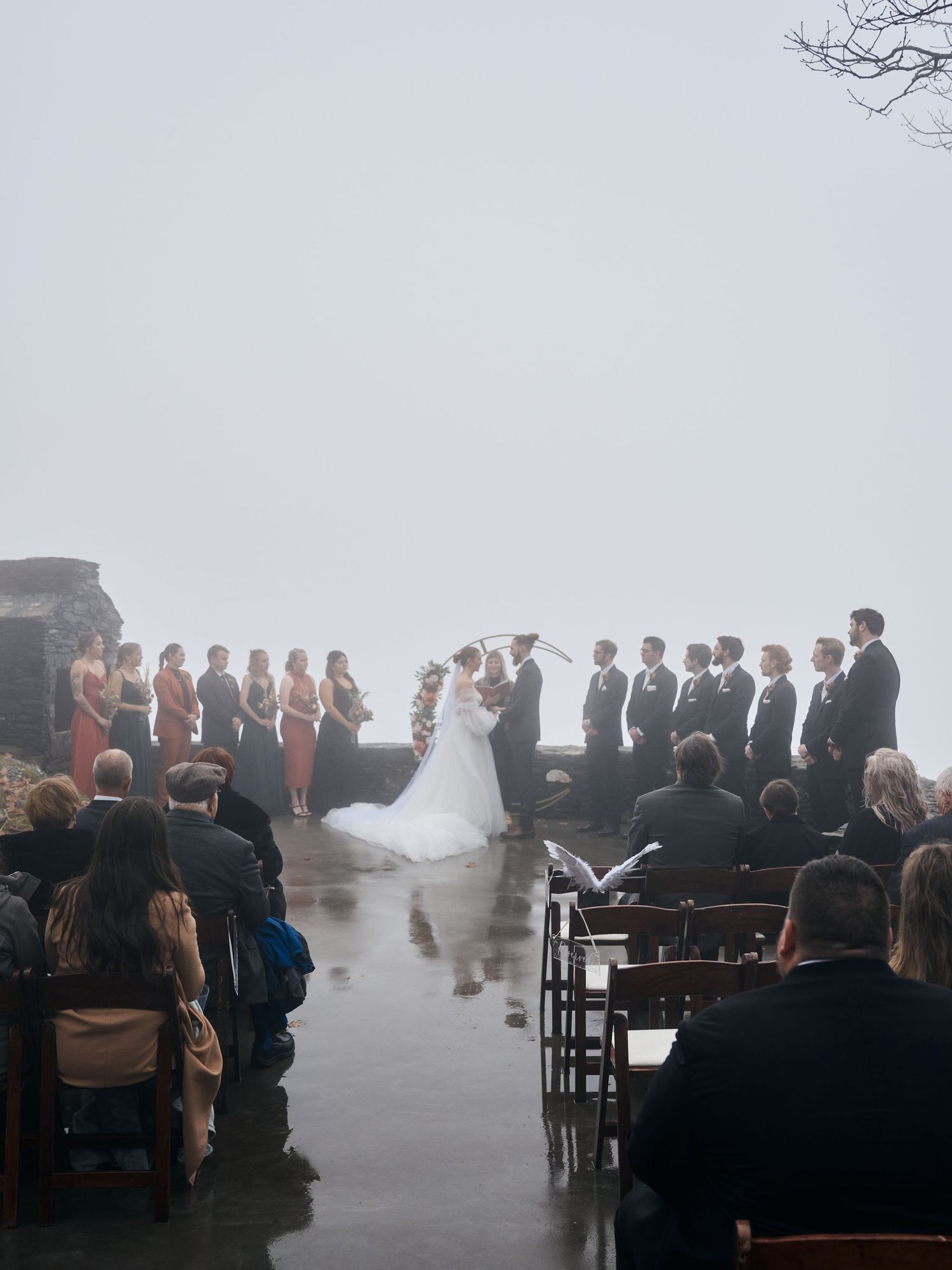 A misty outdoor wedding ceremony with guests seated in rows overlooking a dramatic landscape.