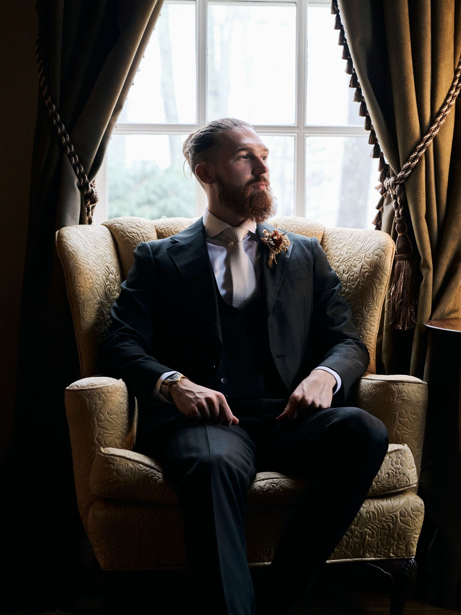 A formal portrait in a luxurious room with velvet curtains and natural window light.