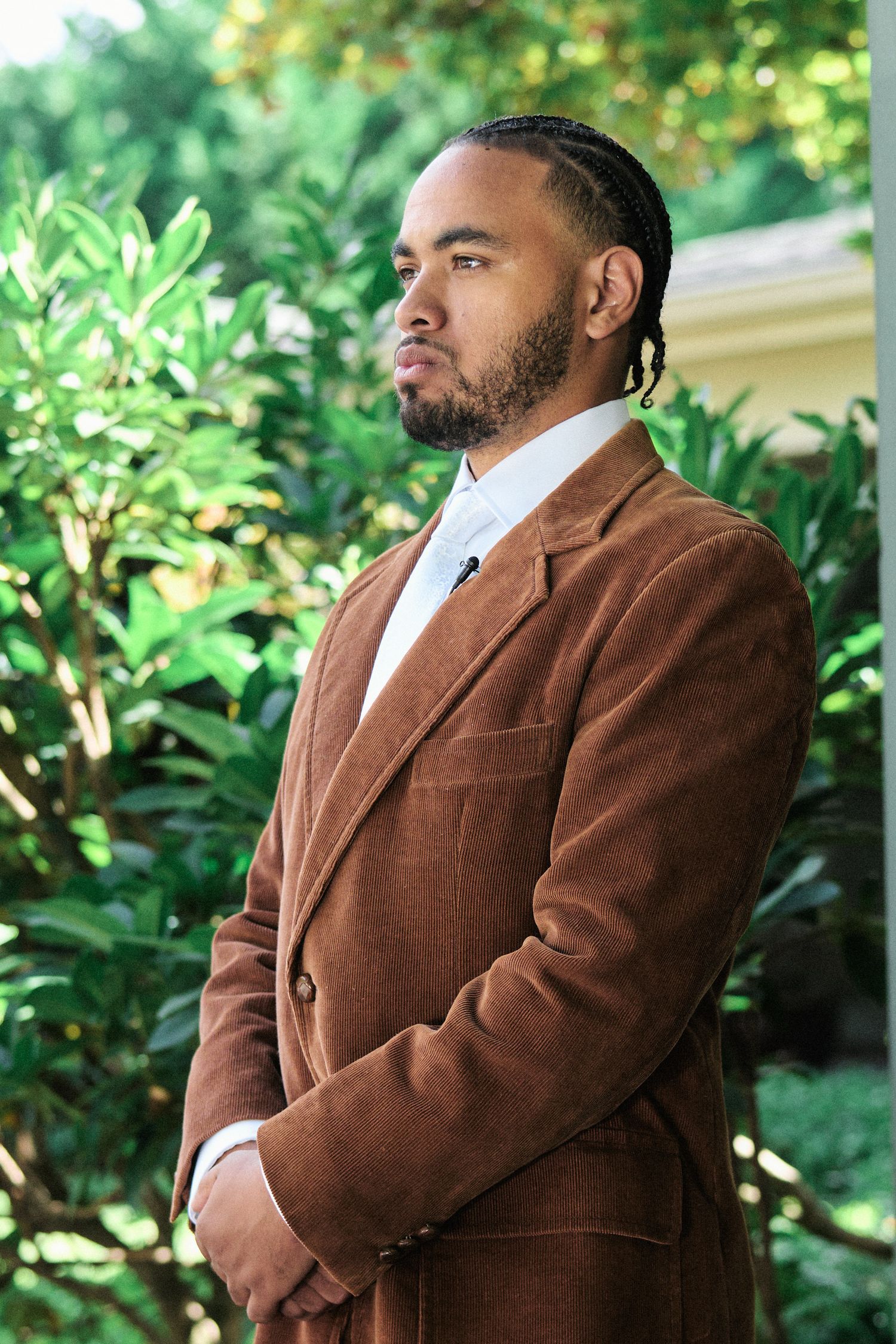 Professional portrait of person in brown corduroy suit against lush garden background.