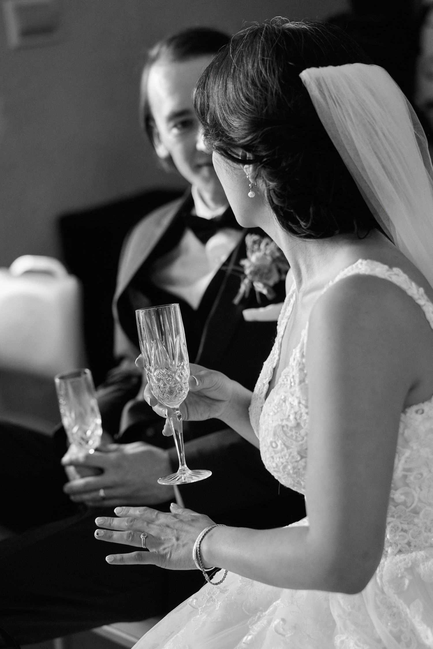 A black and white photo of newlyweds holding champagne glasses during their wedding celebration.