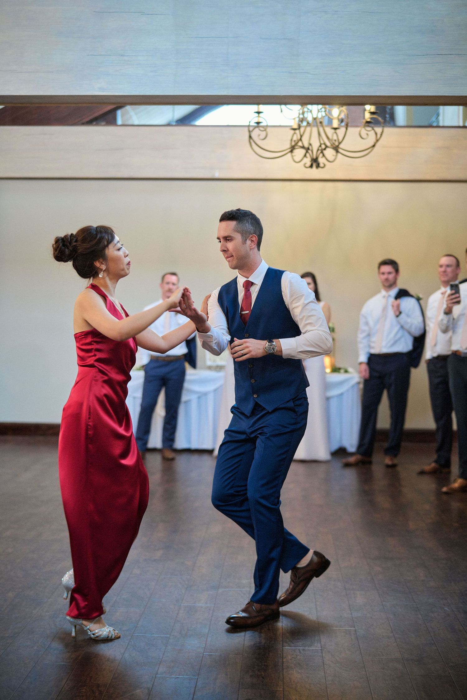 A couple dances together at a wedding reception, with the woman wearing red and man in navy suit.
