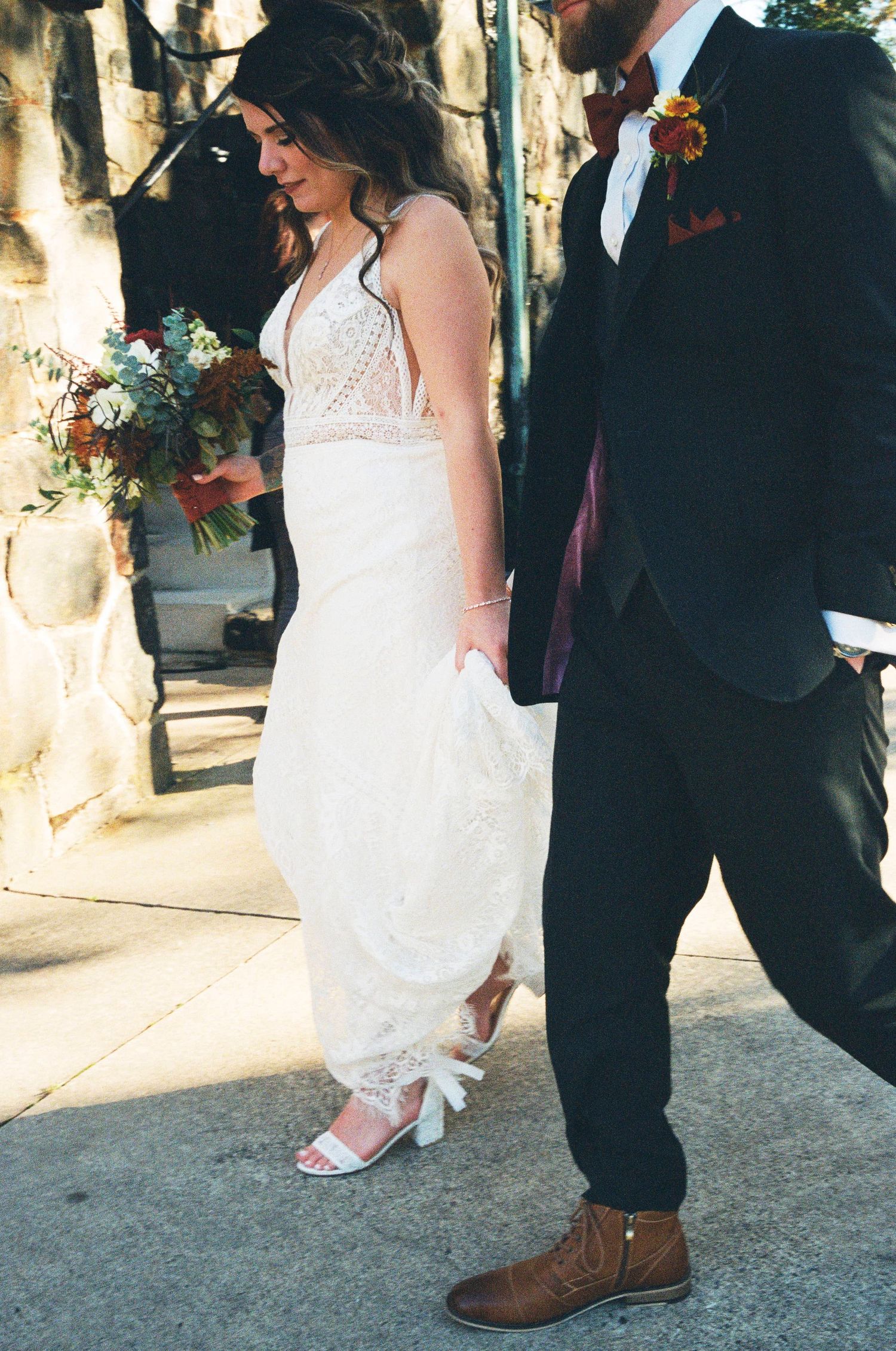 A couple at a wedding with the bride lifting her white dress to show her shoes and the groom in a dark suit.