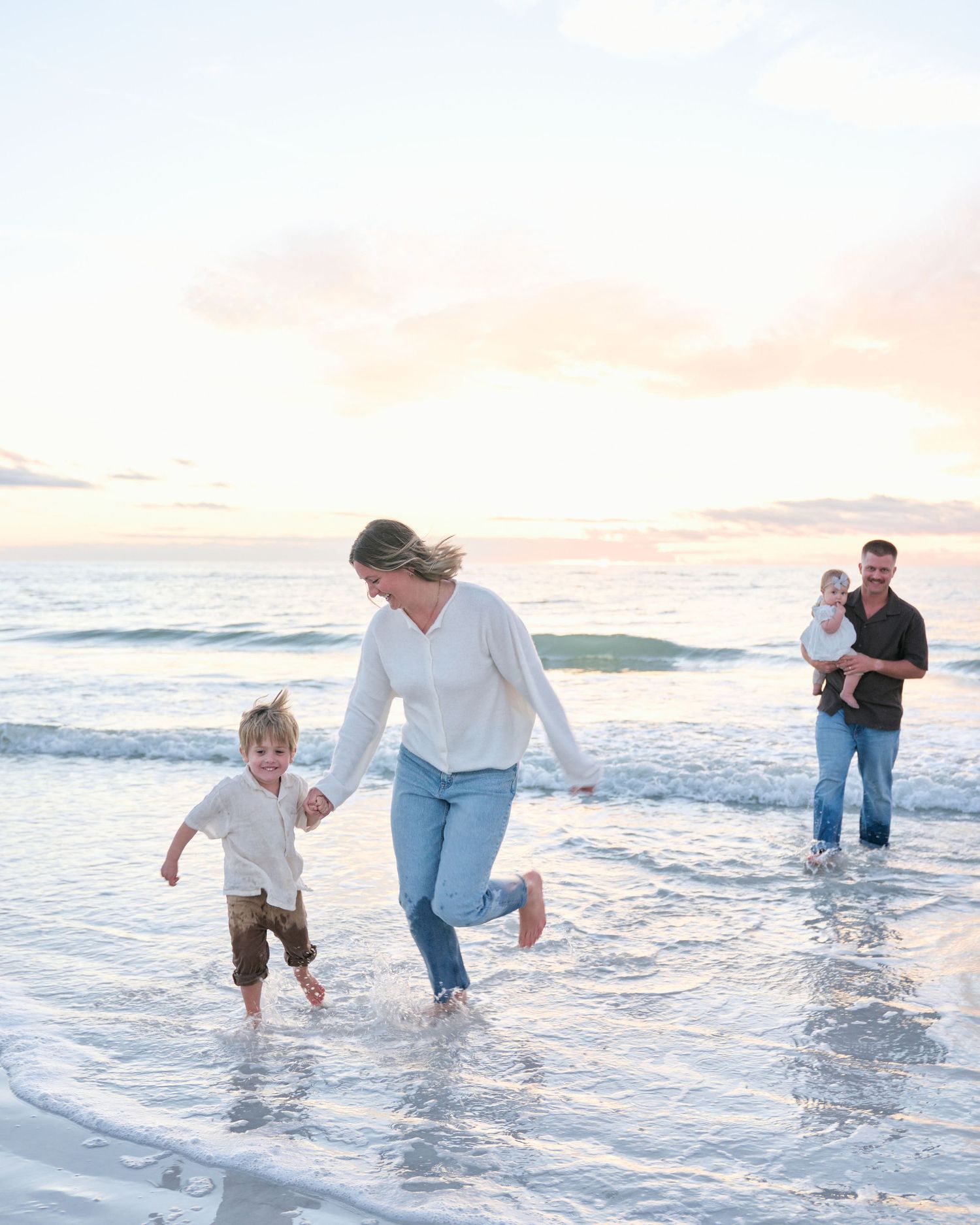 A playful family splashes and runs through ocean waves at sunset along a sandy beach.