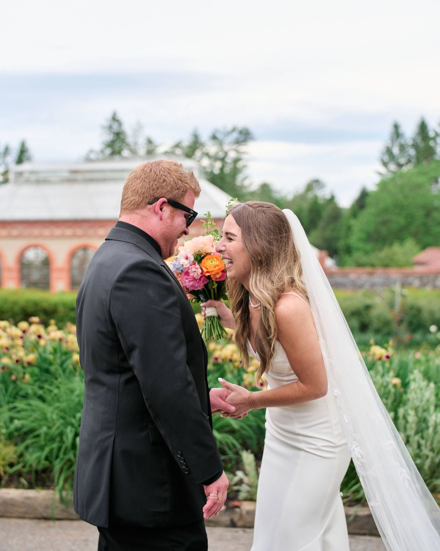 A couple shares a sweet moment in a garden setting during their wedding celebration, surrounded by blooming flowers.