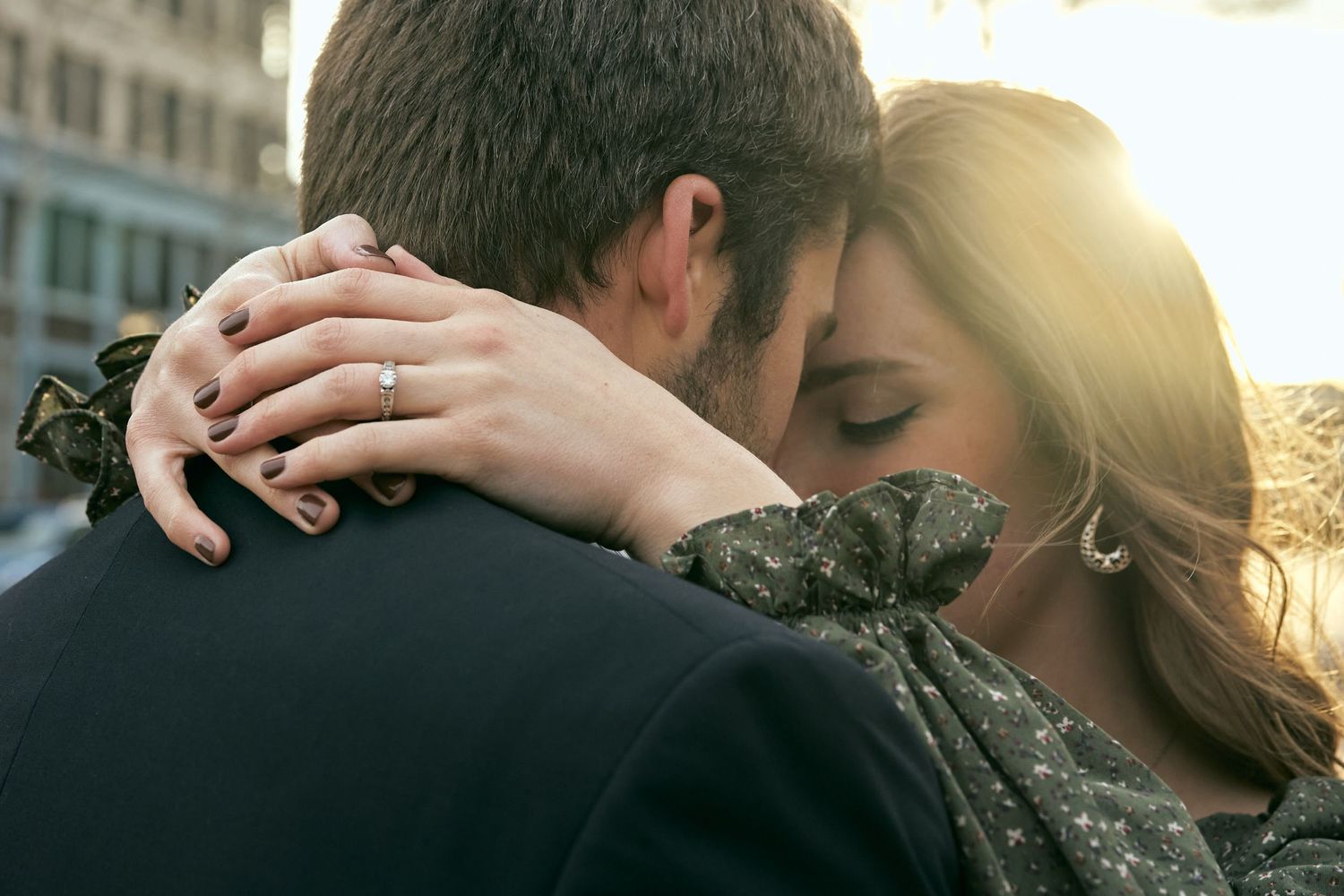 An intimate embrace captured in warm sunlight against an urban backdrop.