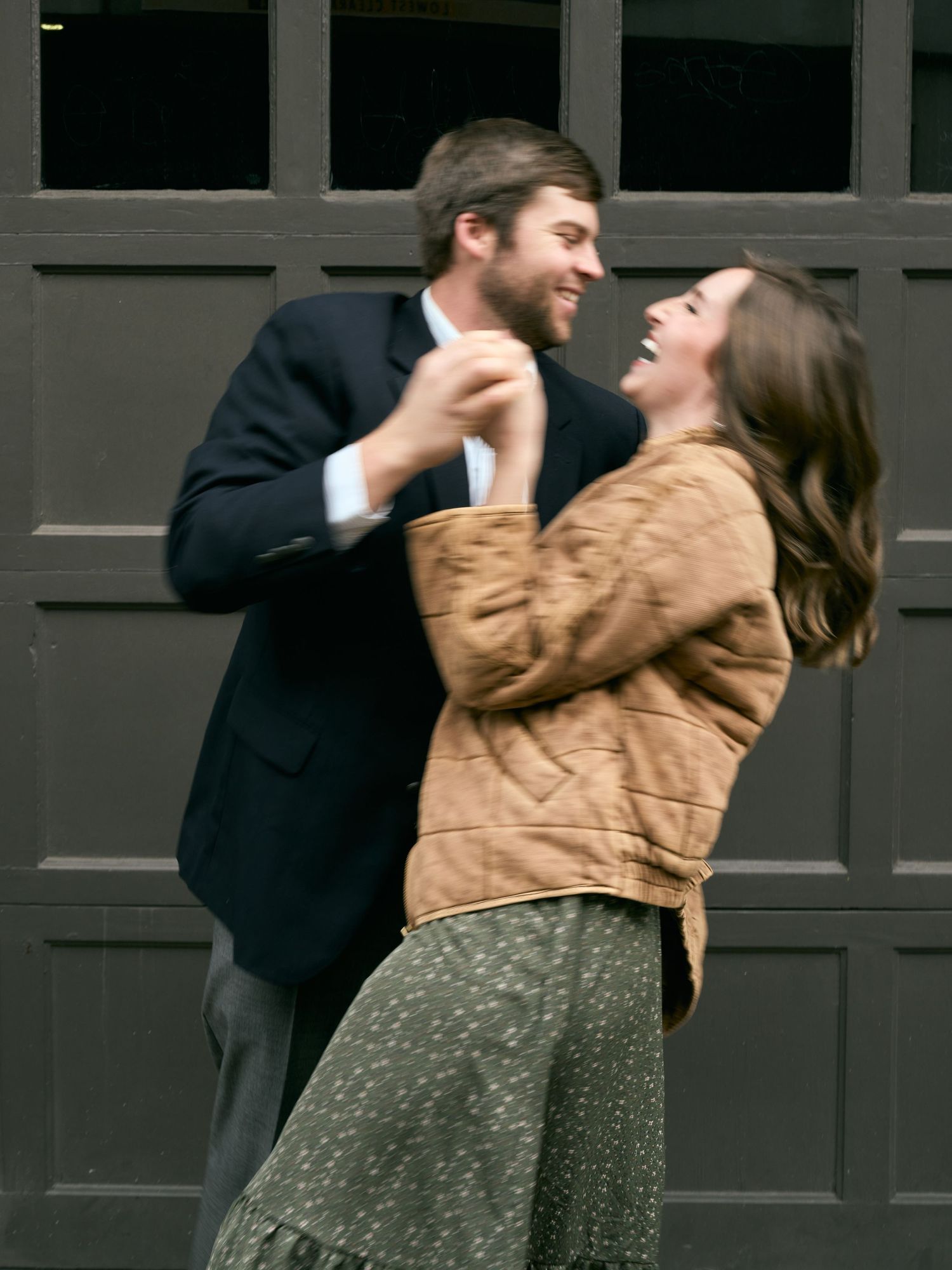 A couple shares a joyful dancing embrace in front of a dark door.