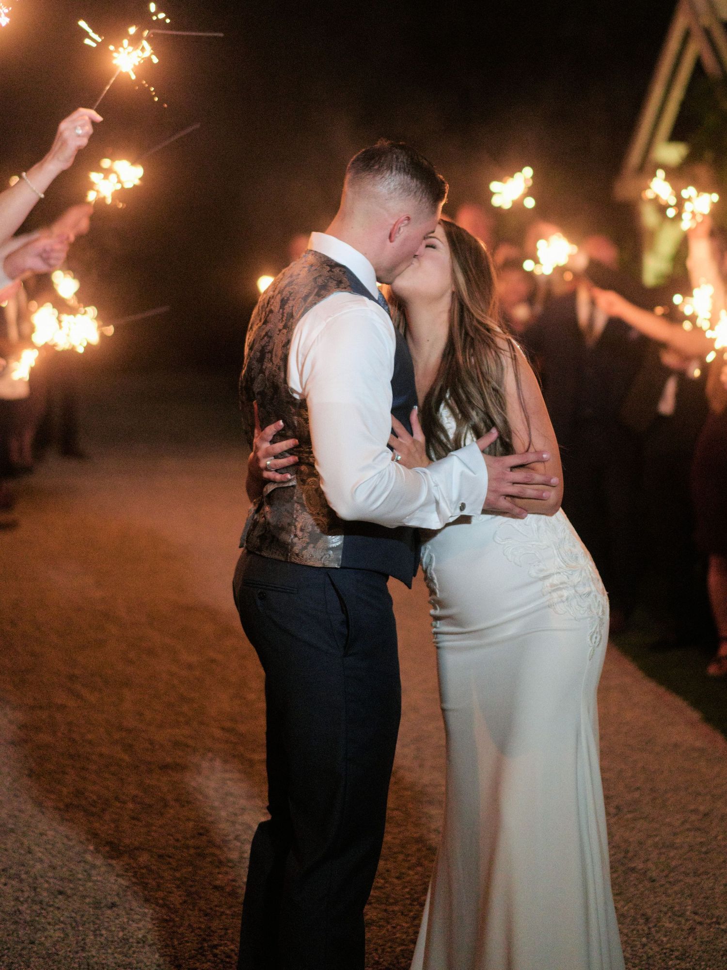 A romantic kiss during a sparkler exit at a nighttime wedding celebration.