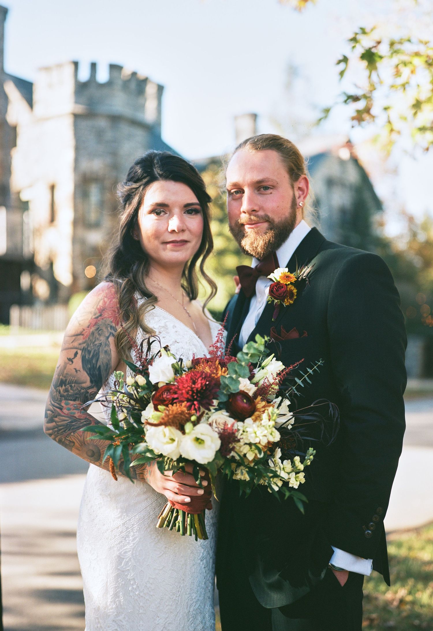 Wedding couple poses with vibrant fall bouquet against stone castle backdrop.