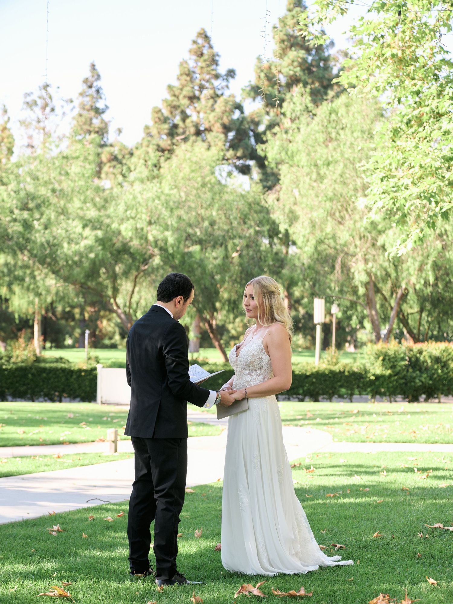A wedding couple shares an intimate moment while reading vows in a sunlit garden.