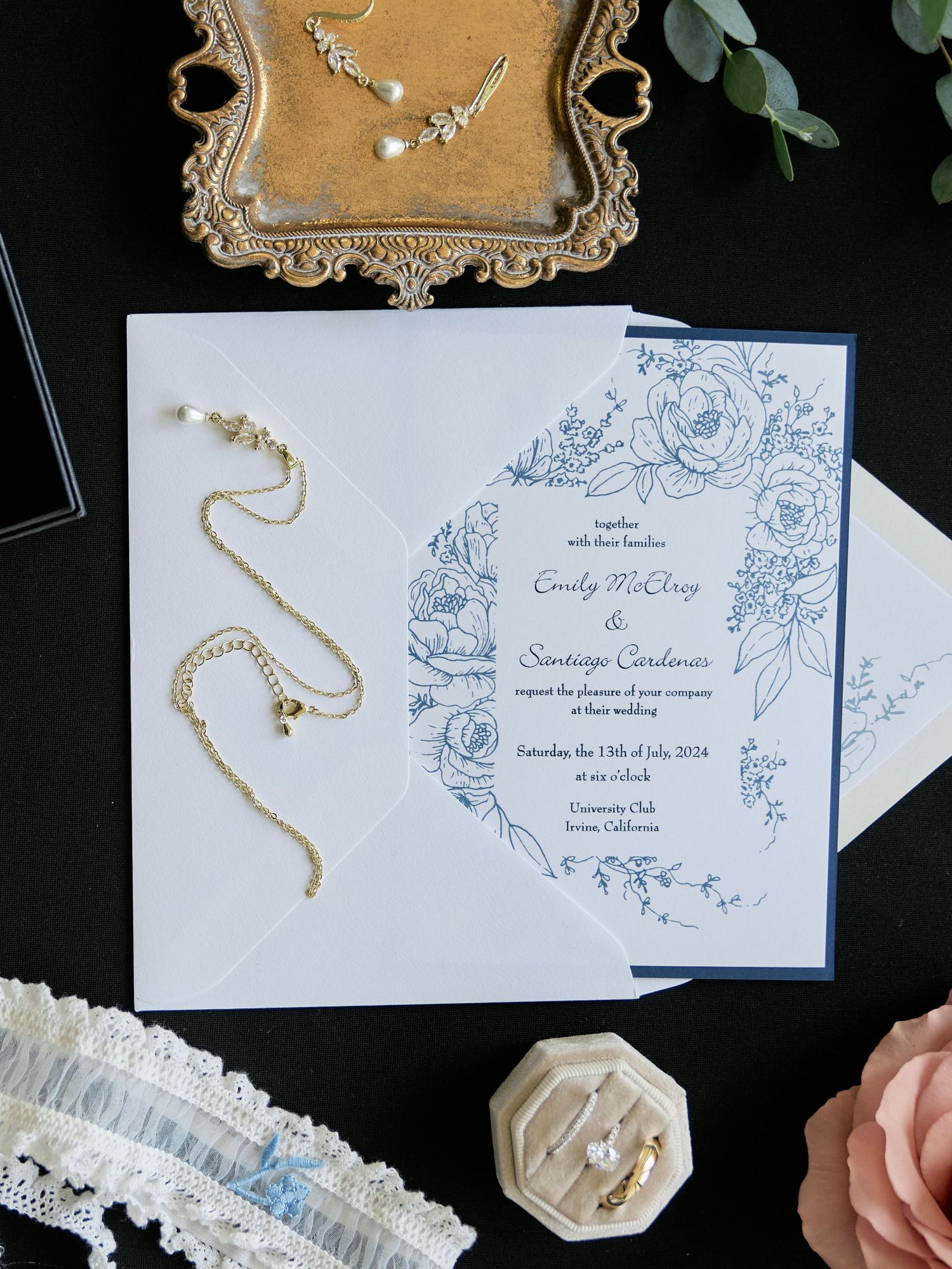Elegant wedding invitation with blue floral design alongside delicate jewelry and lace details.