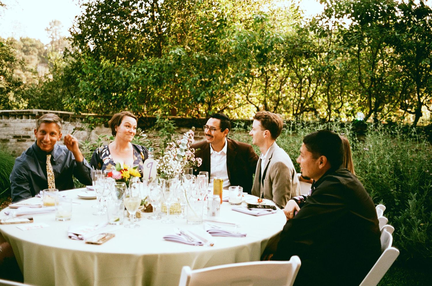 Wedding guests dining at round table during outdoor garden reception.