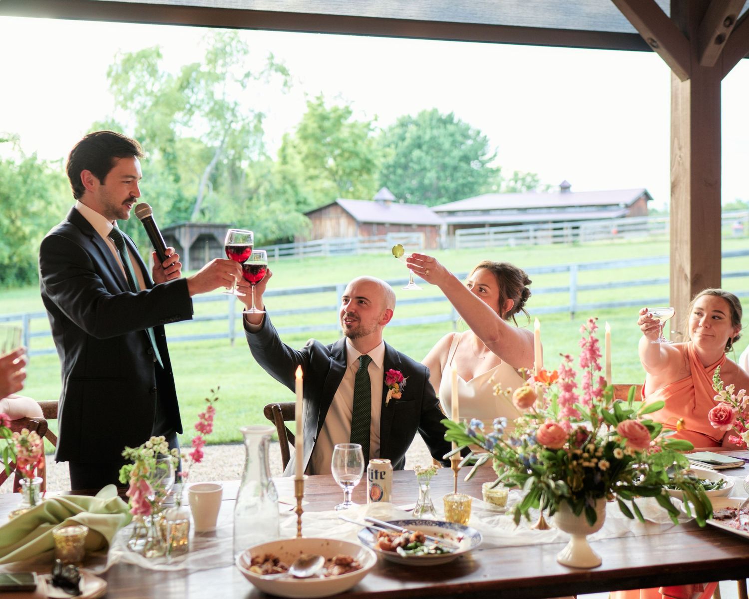Wedding reception toast under a wooden pavilion with floral centerpieces.