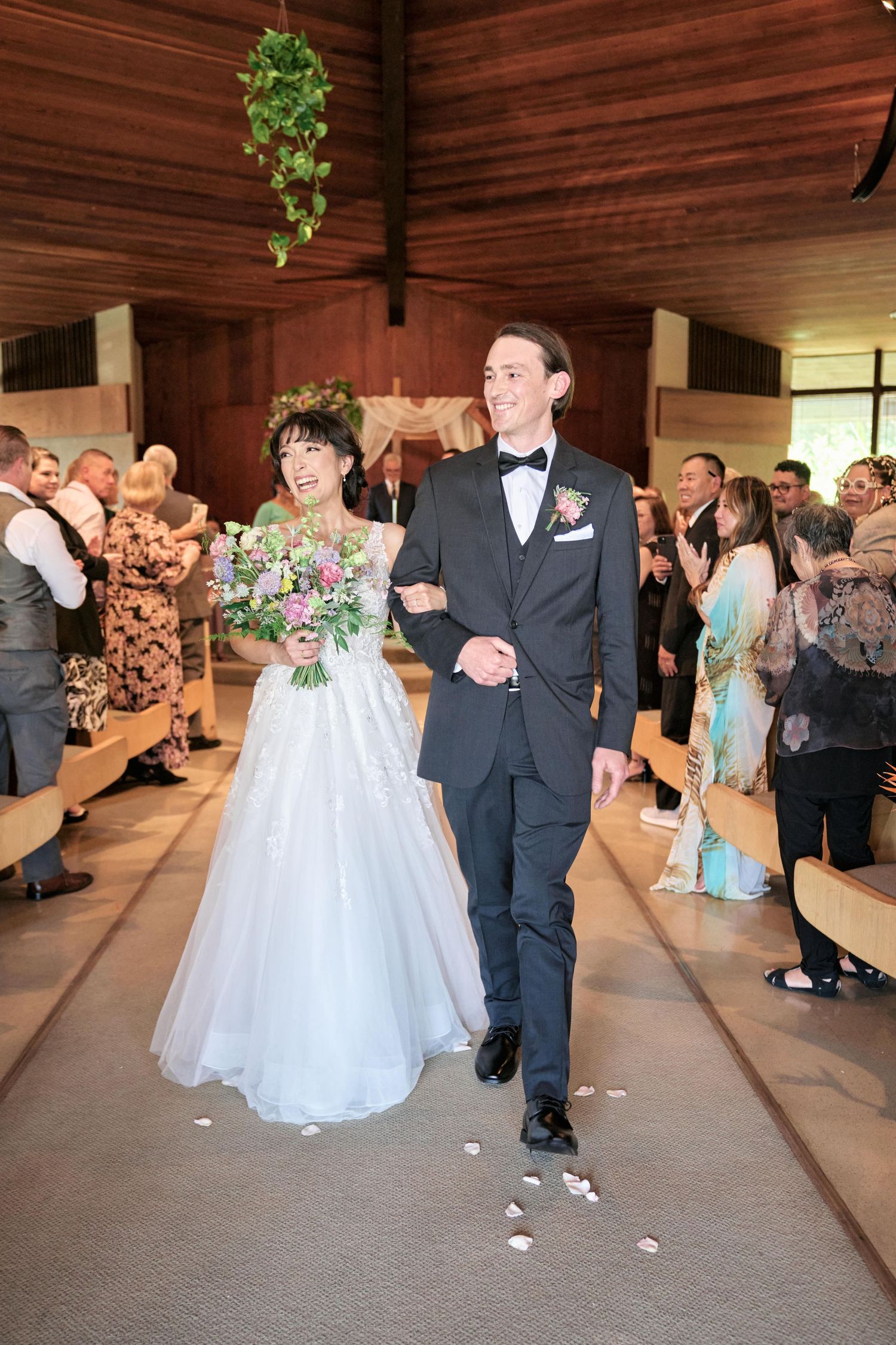 Newlyweds walk down the aisle in a wooden church while guests celebrate their union.
