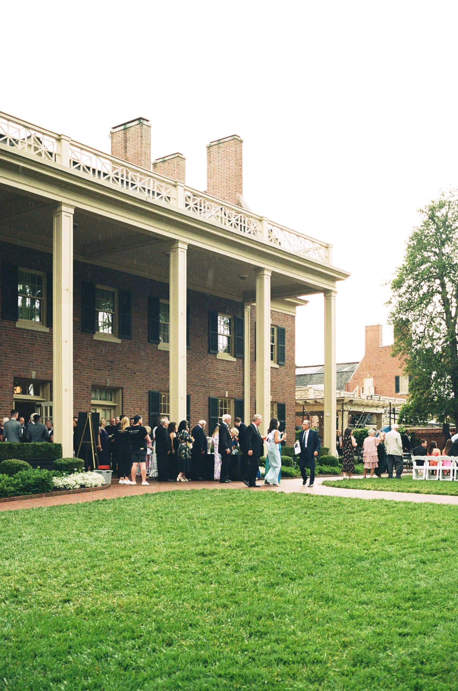 Historic brick mansion with white columns serves as an elegant wedding venue with guests gathered outside.