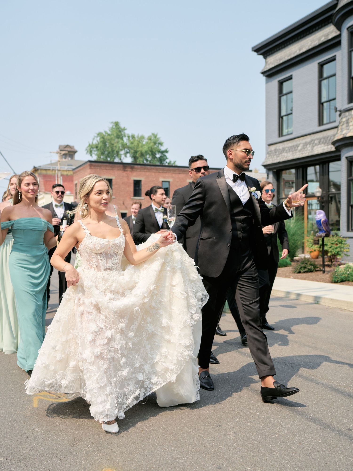Wedding party walks down a street together with attendants in turquoise dresses and black tuxedos.