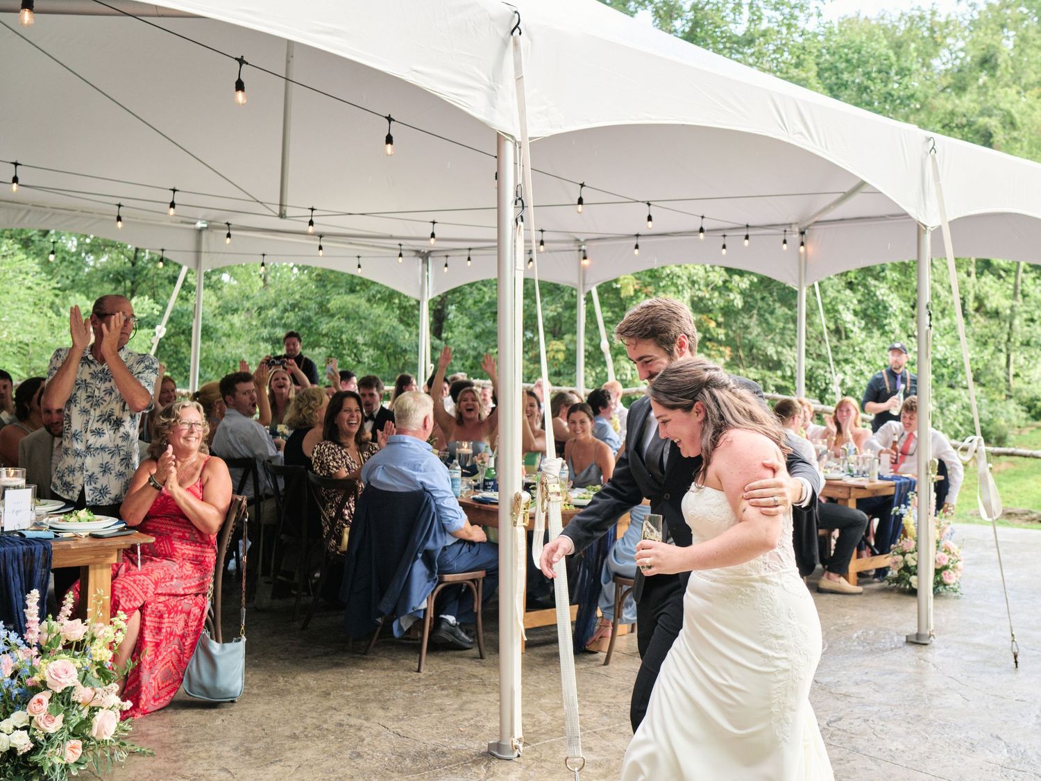 Bride and groom share first dance under white tent with string lights at outdoor wedding reception.