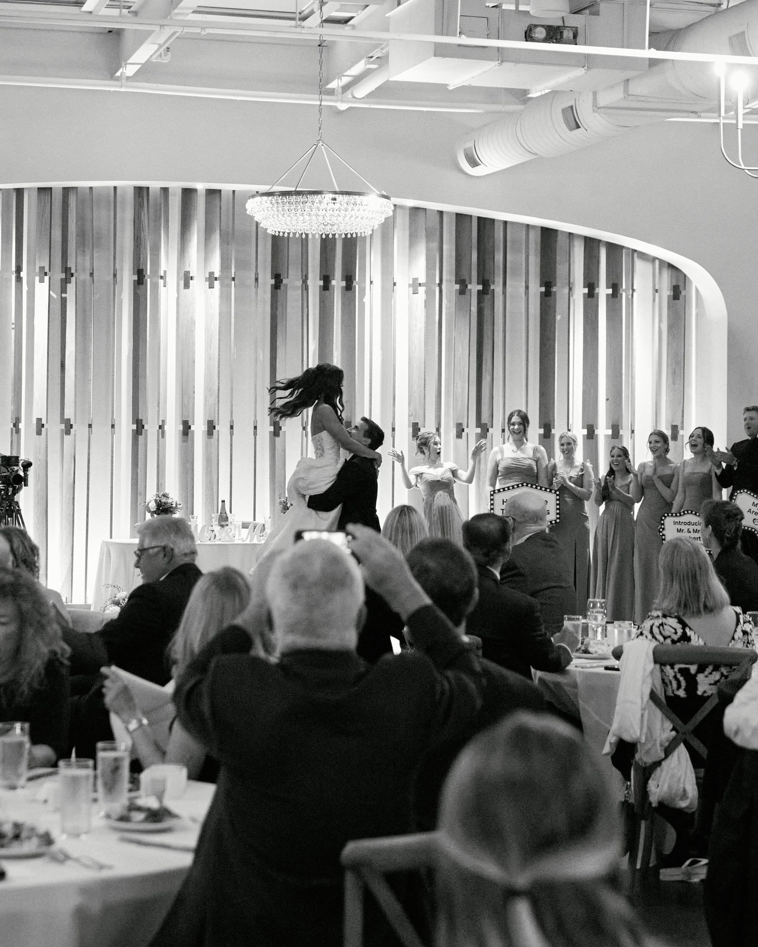 Black and white photo of a groom lifting his bride during their first dance at an elegant wedding reception.