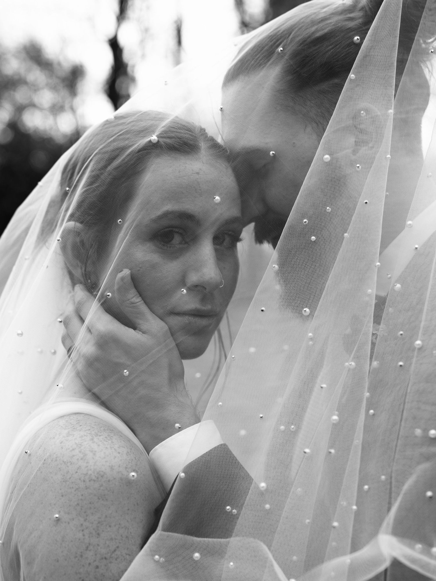 An ethereal black and white portrait through a delicate pearl-adorned wedding veil.
