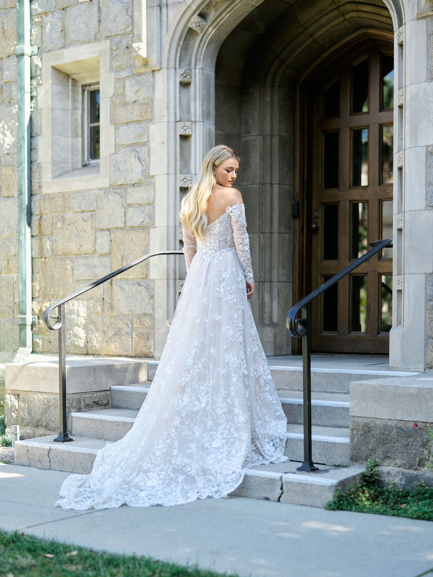 Detailed lace wedding gown with long train photographed at stone church entrance.