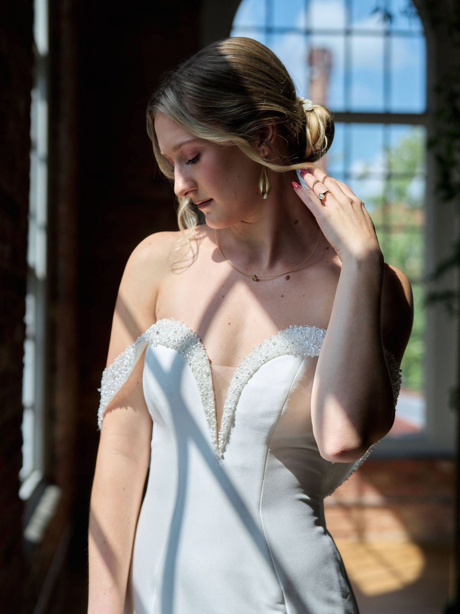 Elegant white wedding dress with delicate lace detailing captured in window light.