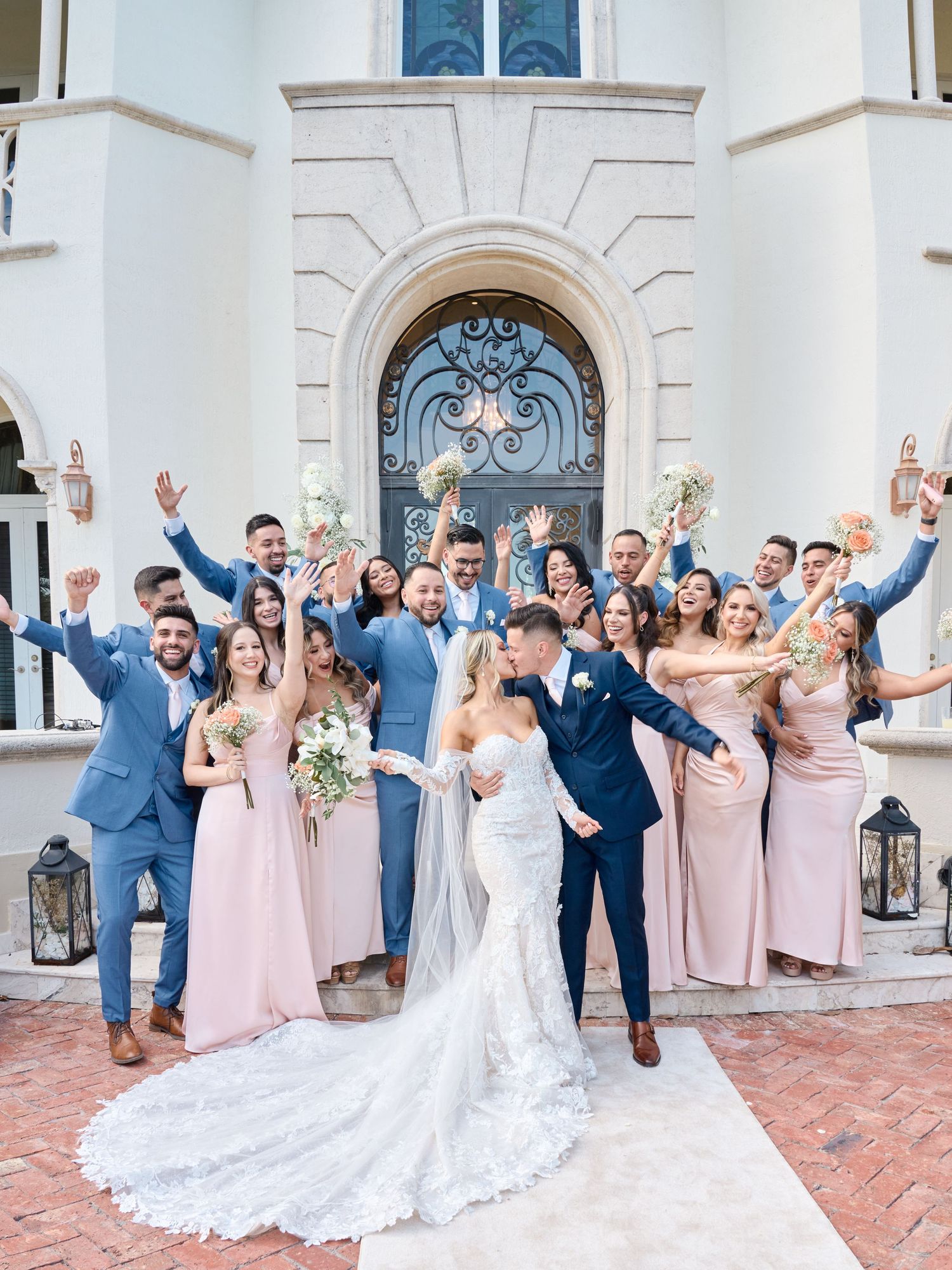 A wedding party celebrates outside a grand white building with elegant architecture.