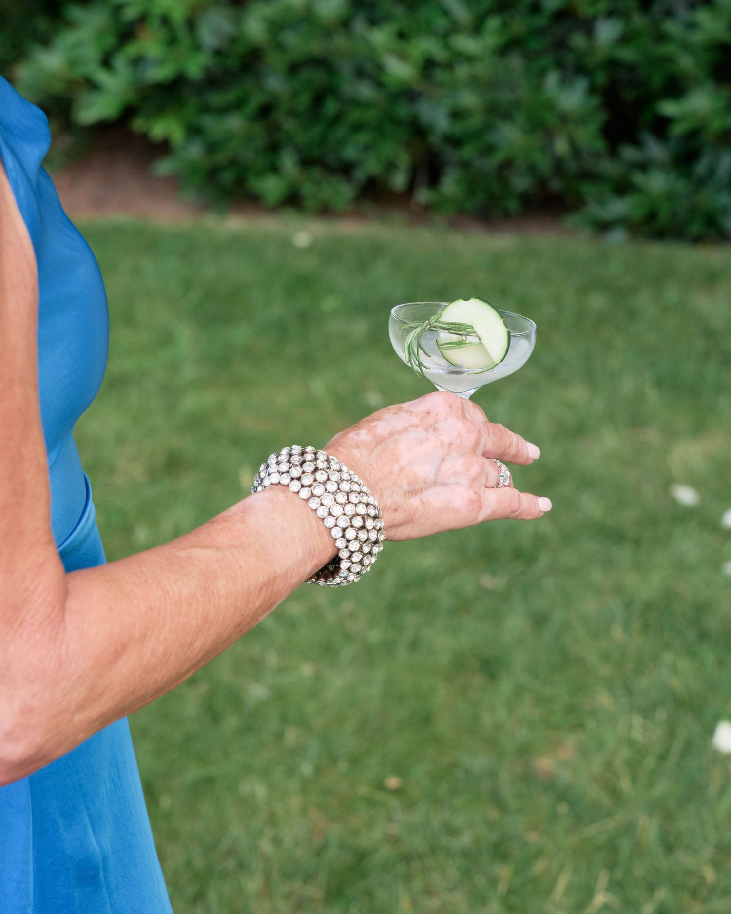 A close-up of a hand wearing a pearl bracelet holding a champagne glass against a green background.