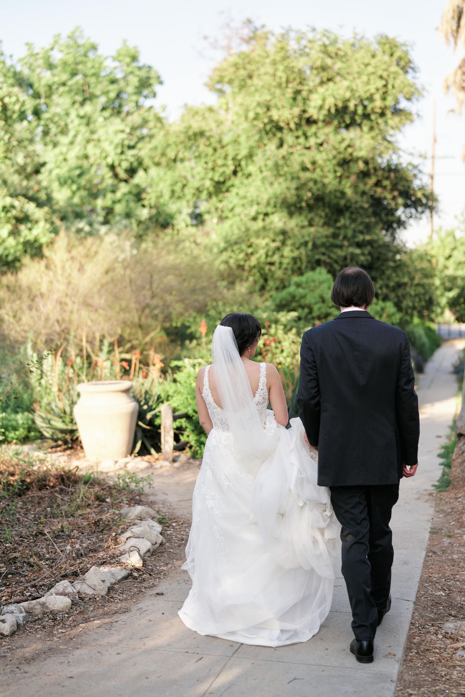 A wedding couple walks down a winding garden path together.