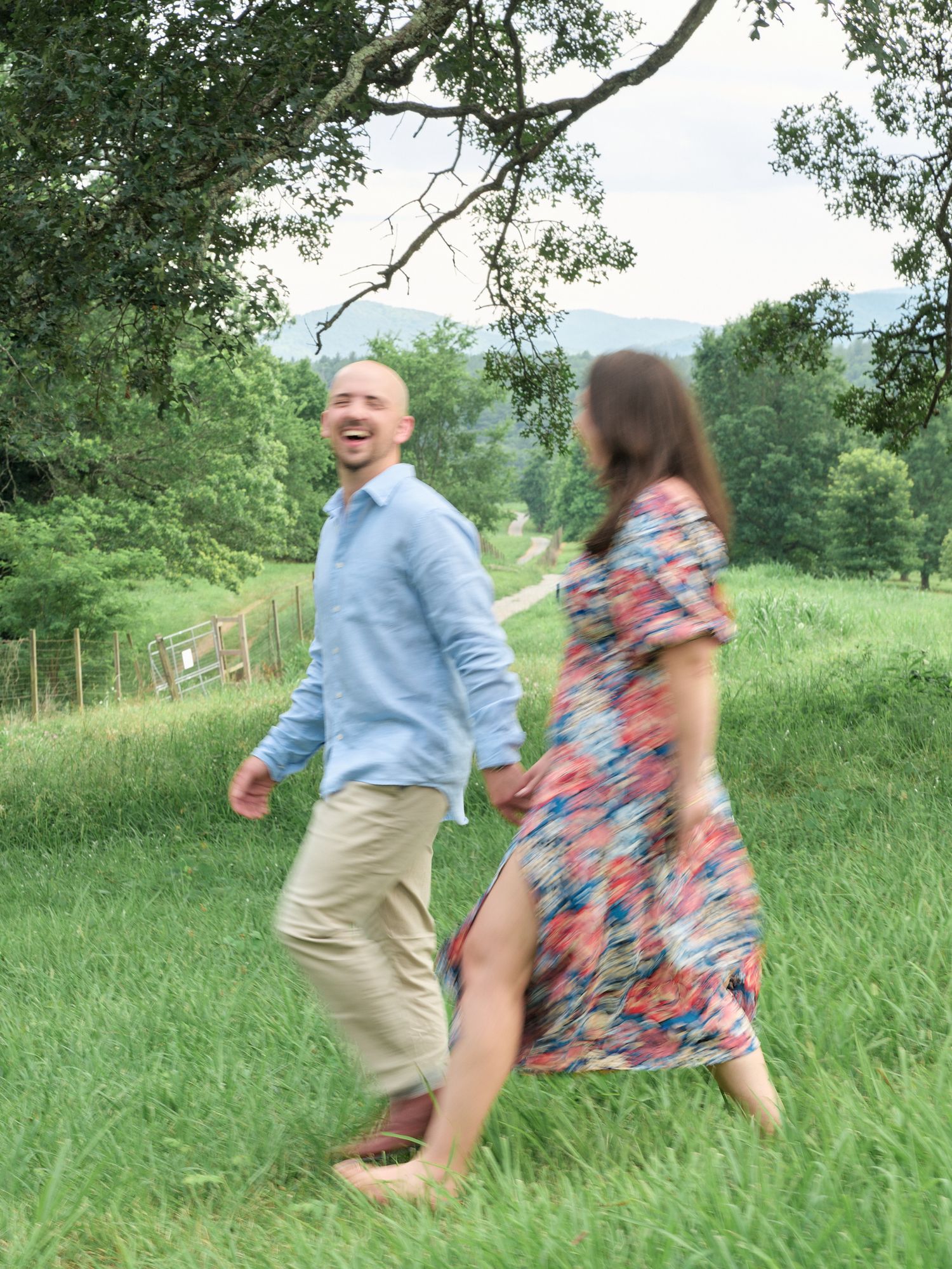 Playful couple running and laughing through tall grass on hillside.