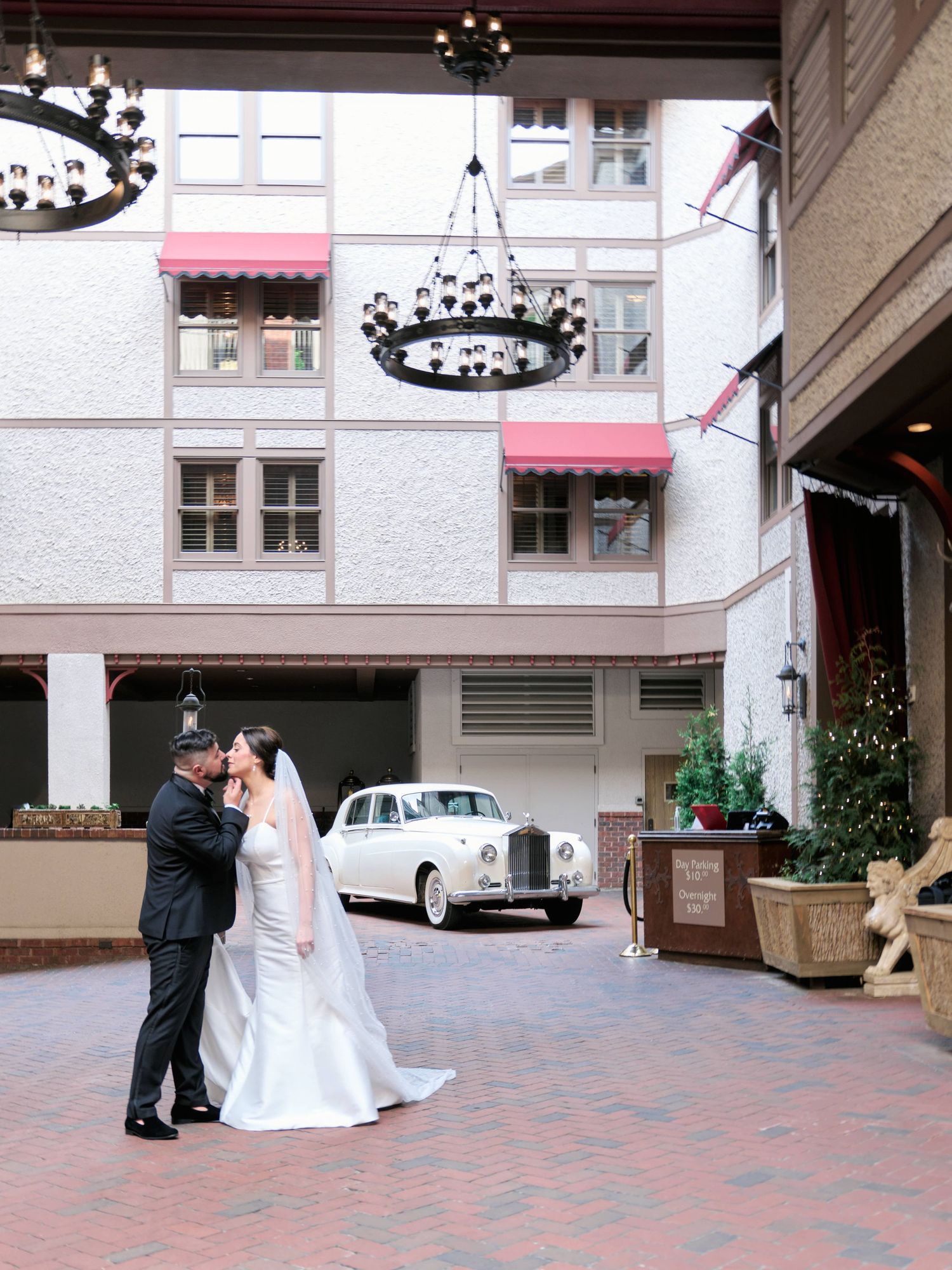 Bride and groom kissing in front of the grand bohemian hotel with a classic car on the background.