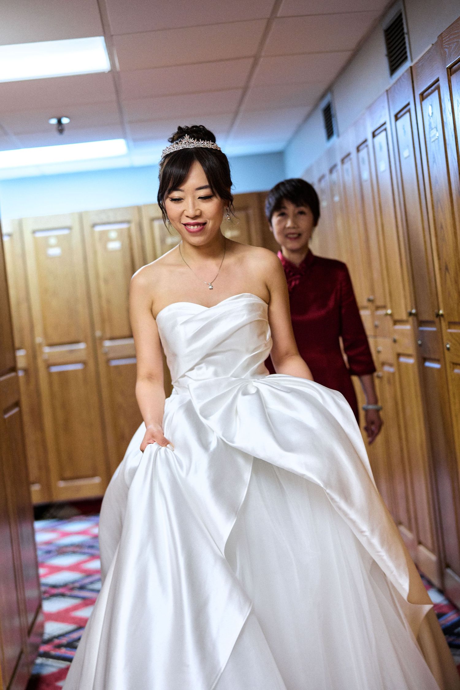 A joyful moment in a locker room hallway showing a bride in a classic ballgown wedding dress.