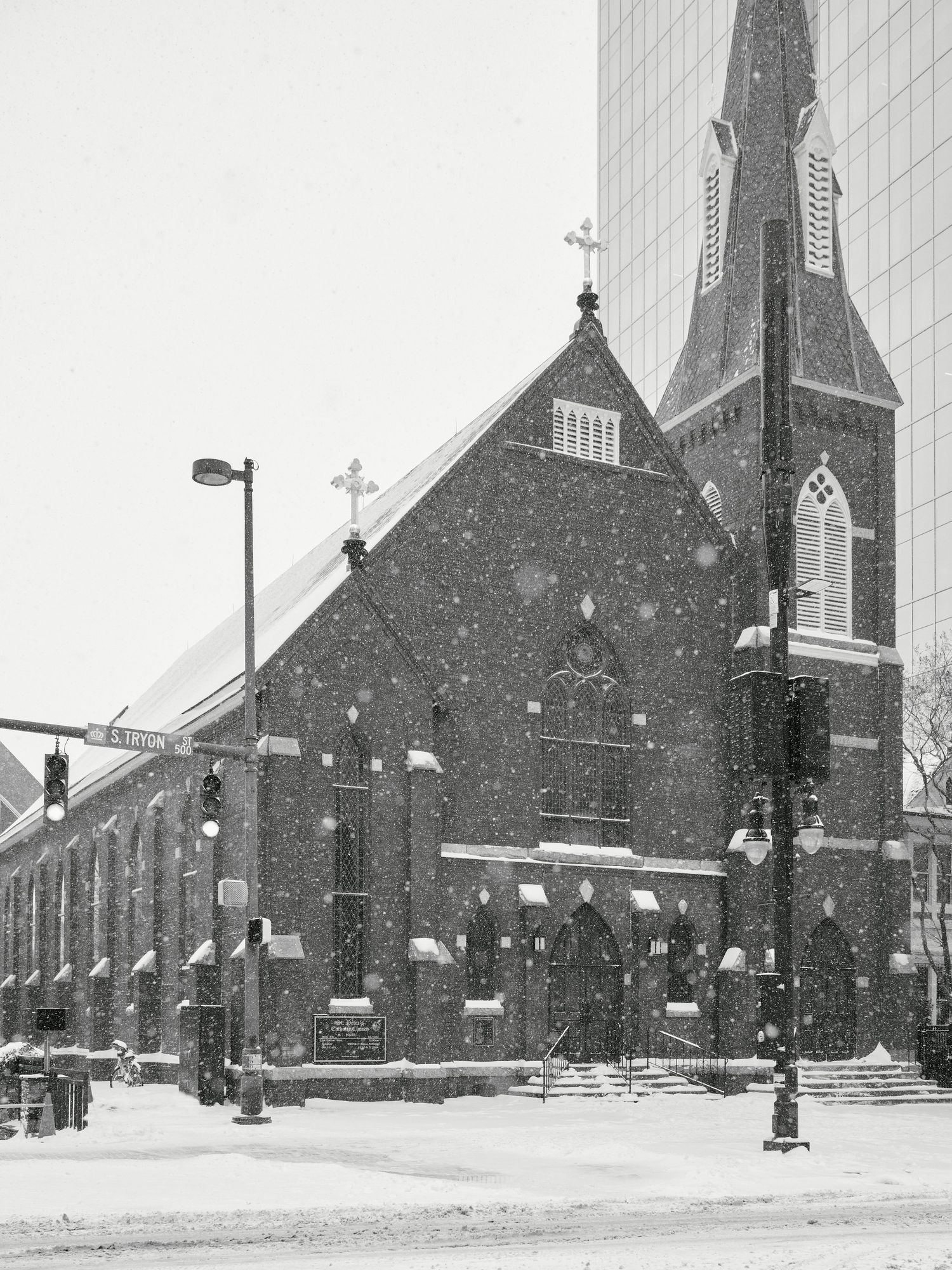Black and white photo of a historic brick church with a steeple during a heavy snowstorm in an urban setting.