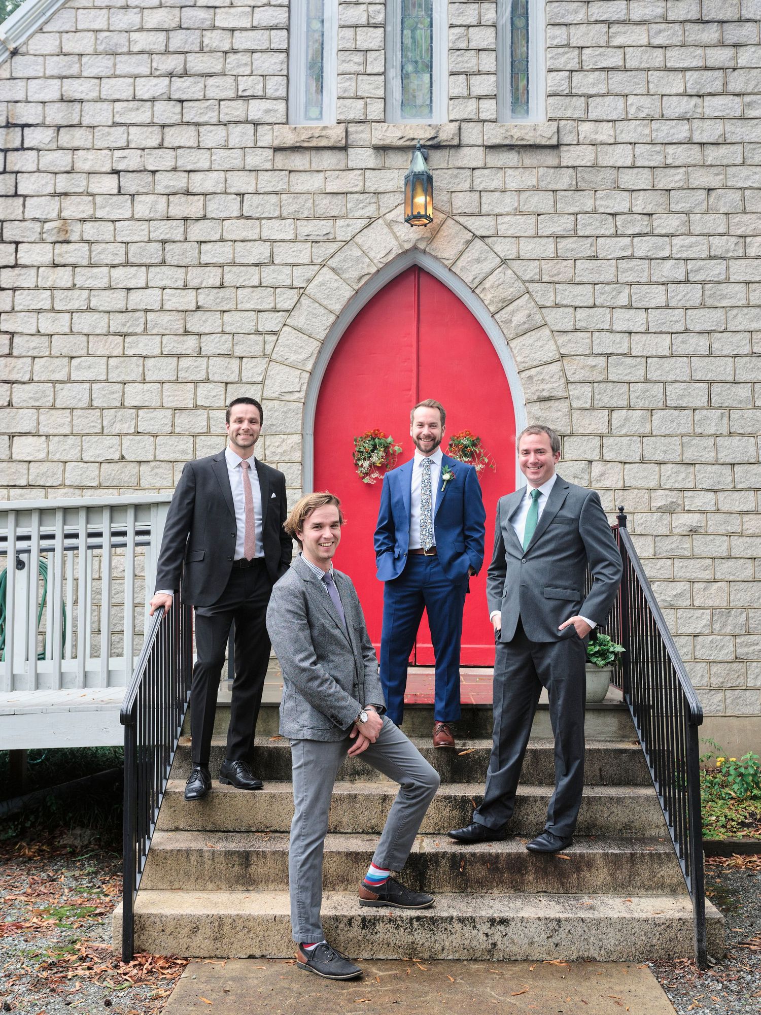 Four people in formal attire pose on stone church steps leading to a red door.