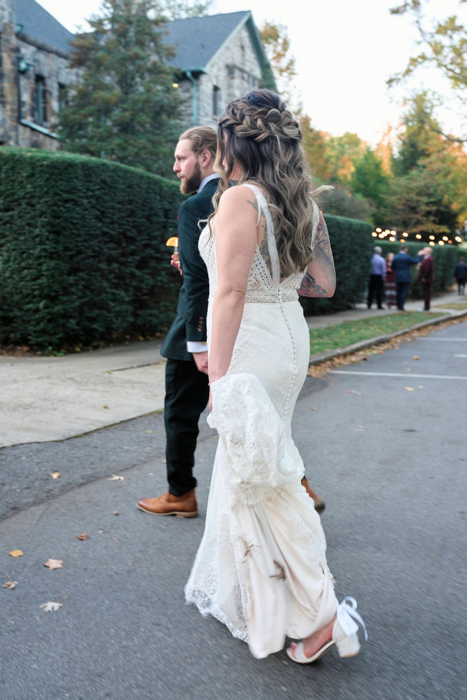 A couple walks along a path near a stone building during their autumn wedding.