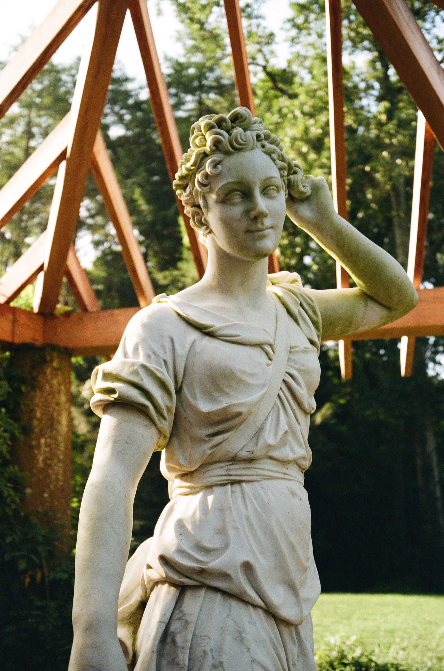 Classic white stone garden statue depicting a graceful female figure in draped clothing against a wooden structure backdrop.
