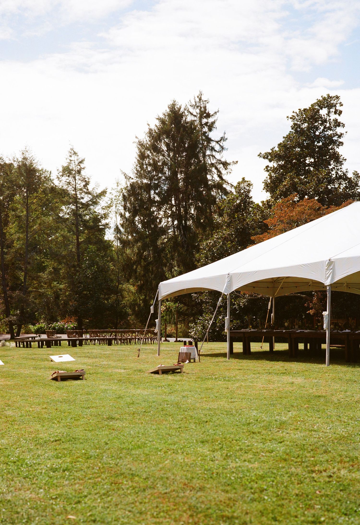 A white event tent setup in a forest clearing with wooden benches arranged in rows.